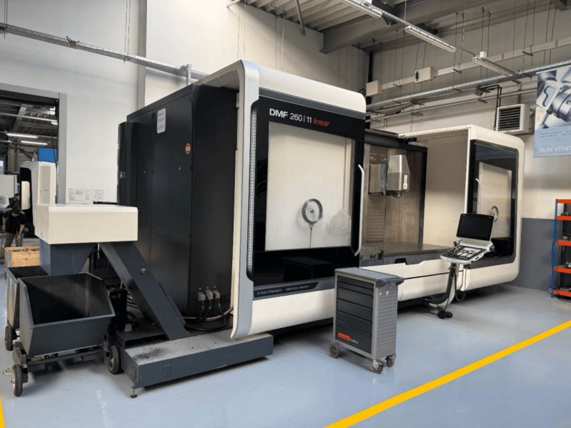 Линейно-фрезерный станок DMG MORI DMF 260 показан спереди, рядом панель управления инструментом и передвижная инструментальная тележка.