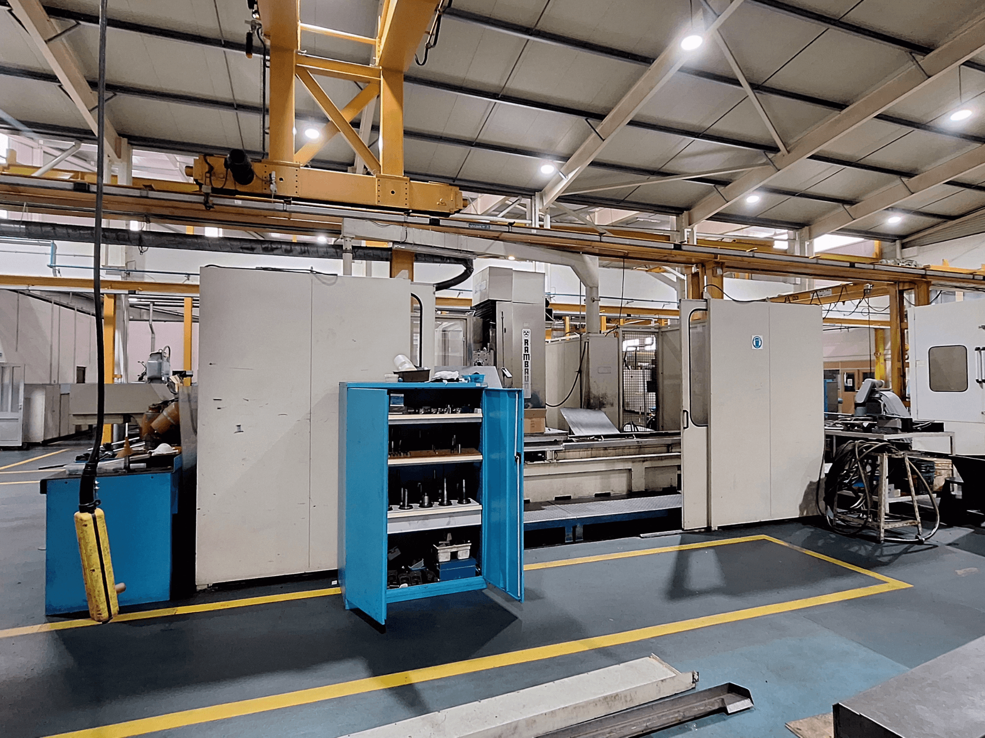 Портальный фрезерный станок Rambaudi RX 1250, вид спереди с хранилищем инструментов, в просторном промышленном рабочем пространстве.