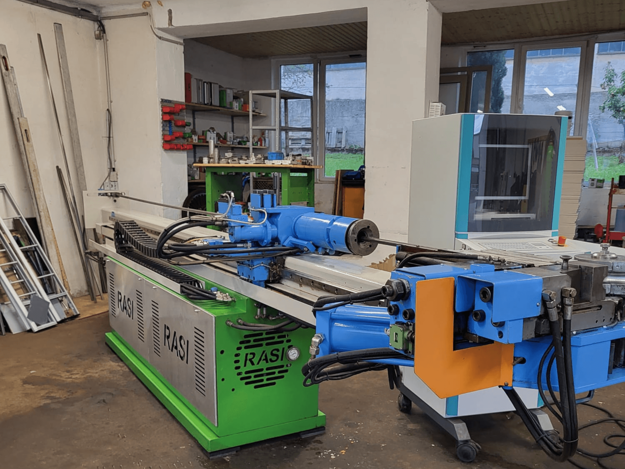 Станок Rasi S 80.6 L G-V3C50 в мастерской, вид сбоку с синими и зелеными компонентами и панелью управления.