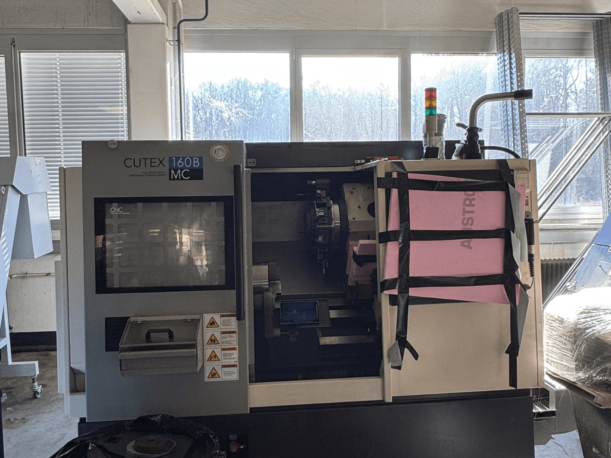 Вид спереди на горизонтальный токарный станок HWACHEON CUTEX 160 B VDI с панелью управления и баком для охлаждающей жидкости, оснащенный сигнальной лампой безопасности.