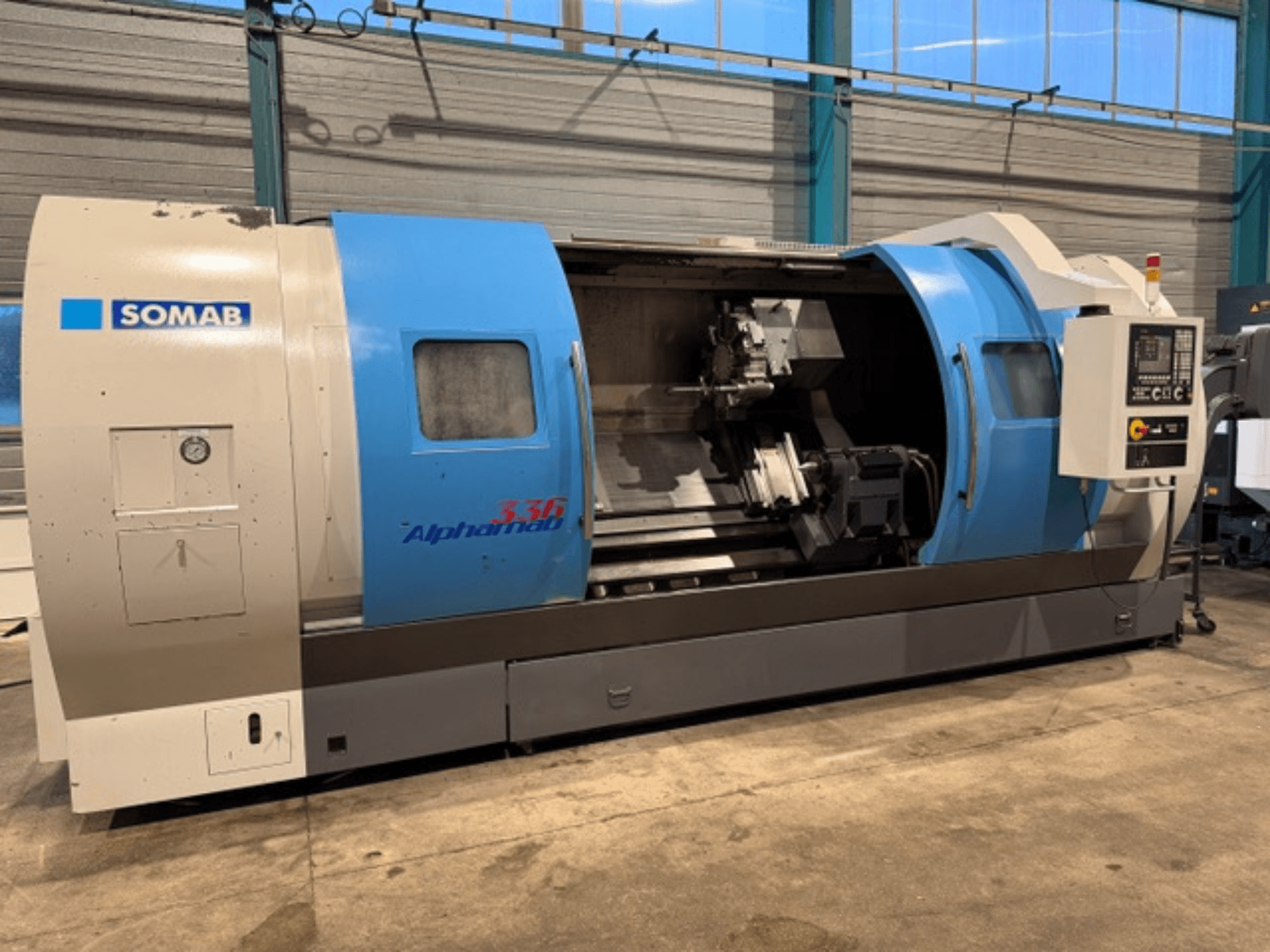 Токарный станок с ЧПУ SOMAB Alpha 336, вид спереди, в сине-сером корпусе и с панелью управления сбоку для управления.