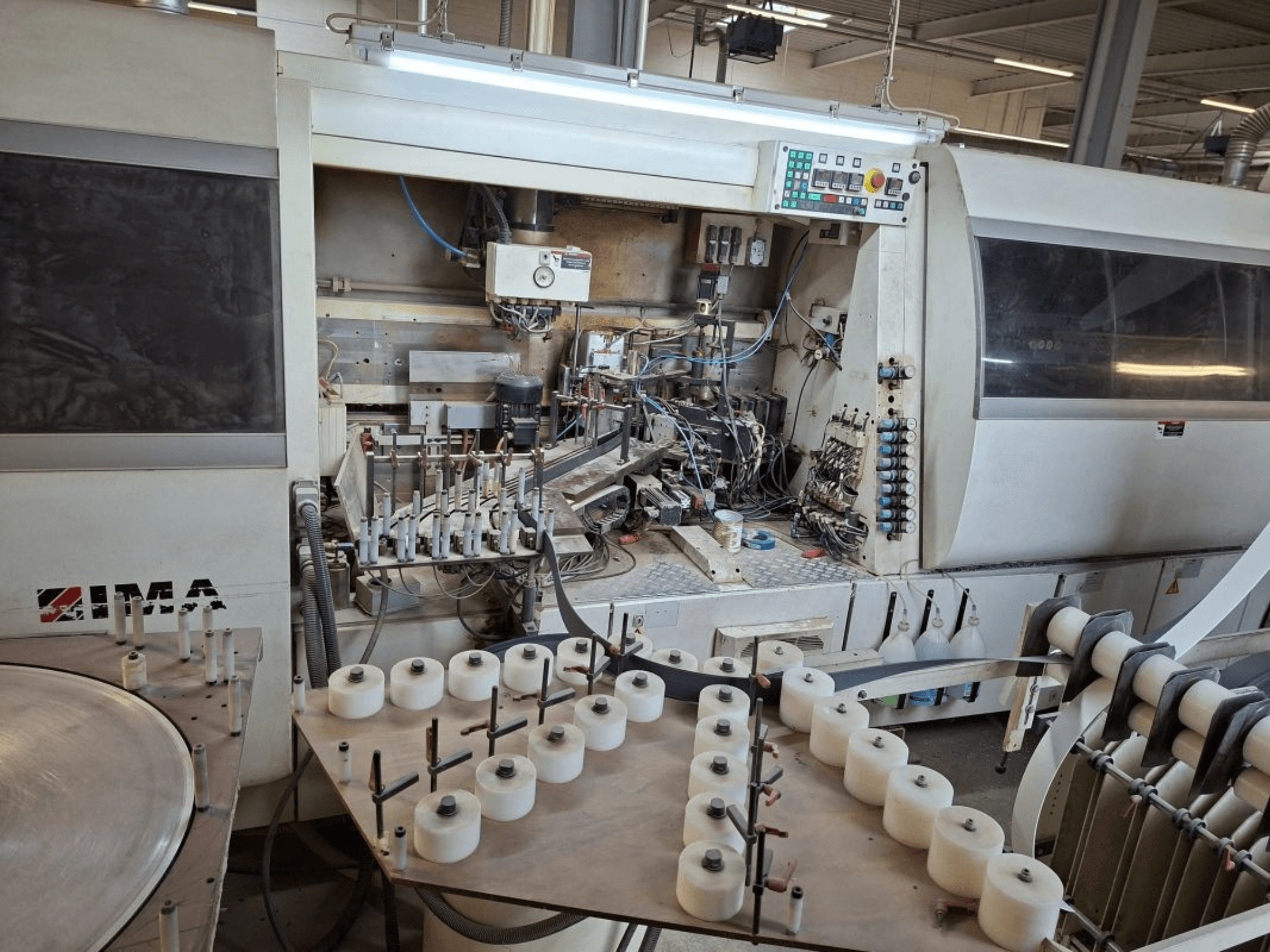 Сбоку видна техника IMA, демонстрирующая сложные механические компоненты и круглый стол с белыми катушками.