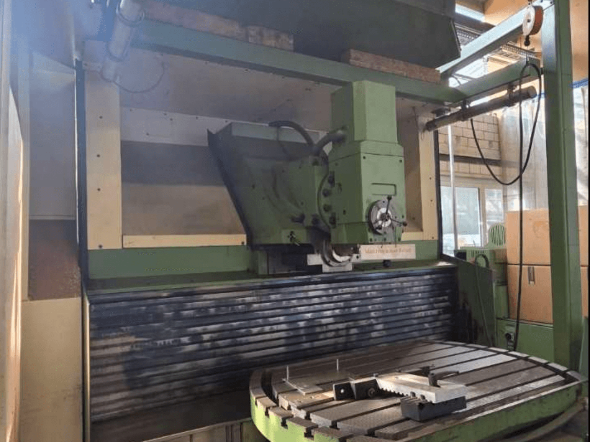 Универсальный обрабатывающий центр MAHO MH1000 C с видом спереди, демонстрирует зеленую конструкцию, шпиндель и поворотный стол с заготовкой.