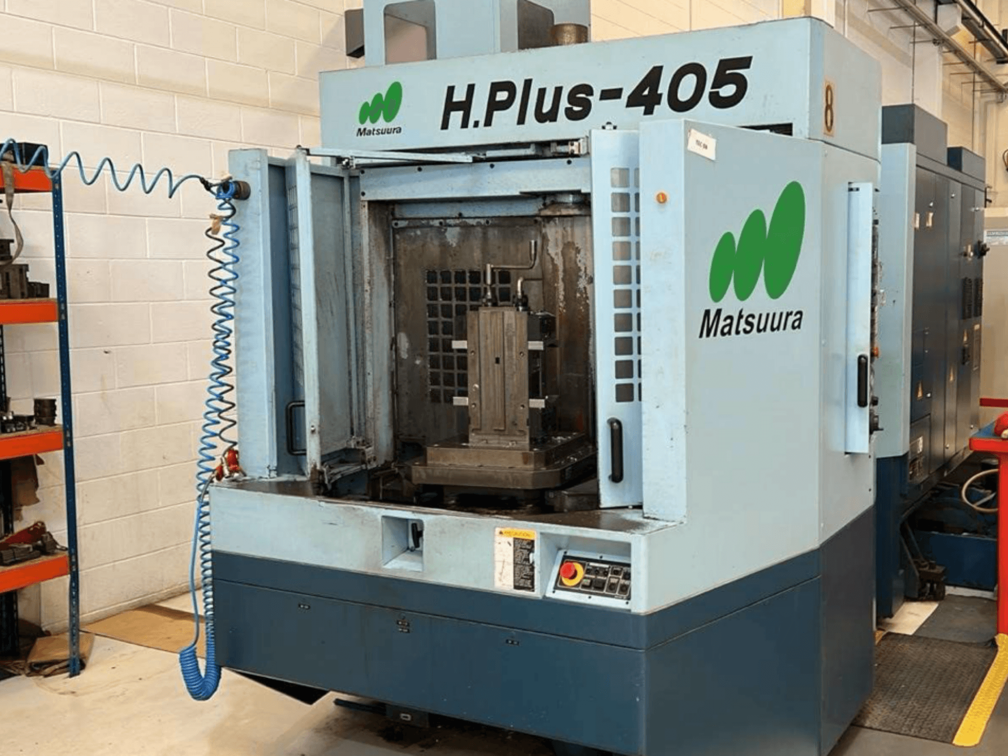 Вид спереди на горизонтальный обрабатывающий центр Matsuura H.Plus 405 с открытой дверью, на котором видны рабочая зона и панель управления.