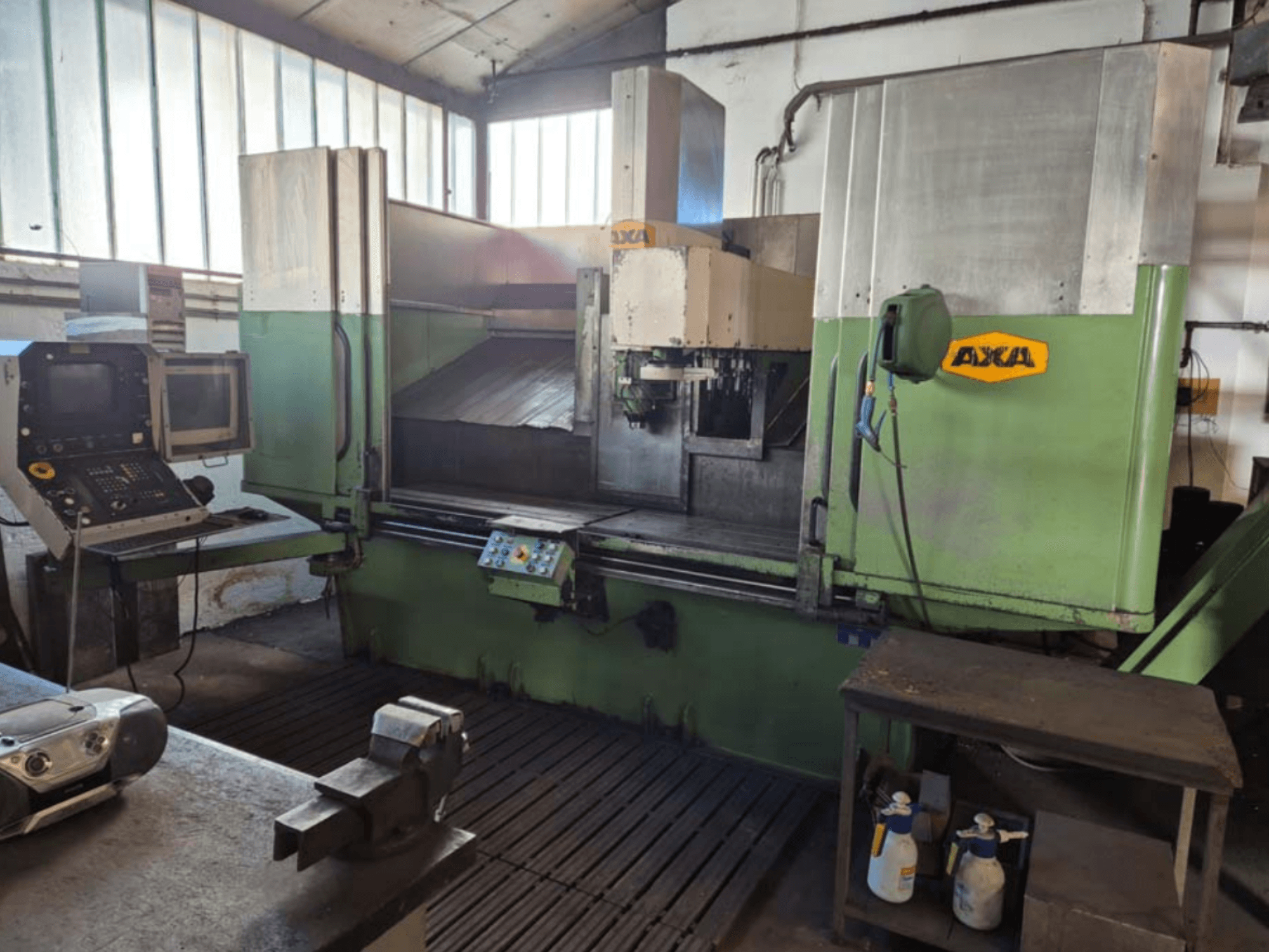 Вертикальный обрабатывающий центр AXA VSC-2M, вид спереди, панель управления и рабочая зона с режущими инструментами и принадлежностями для чистки.