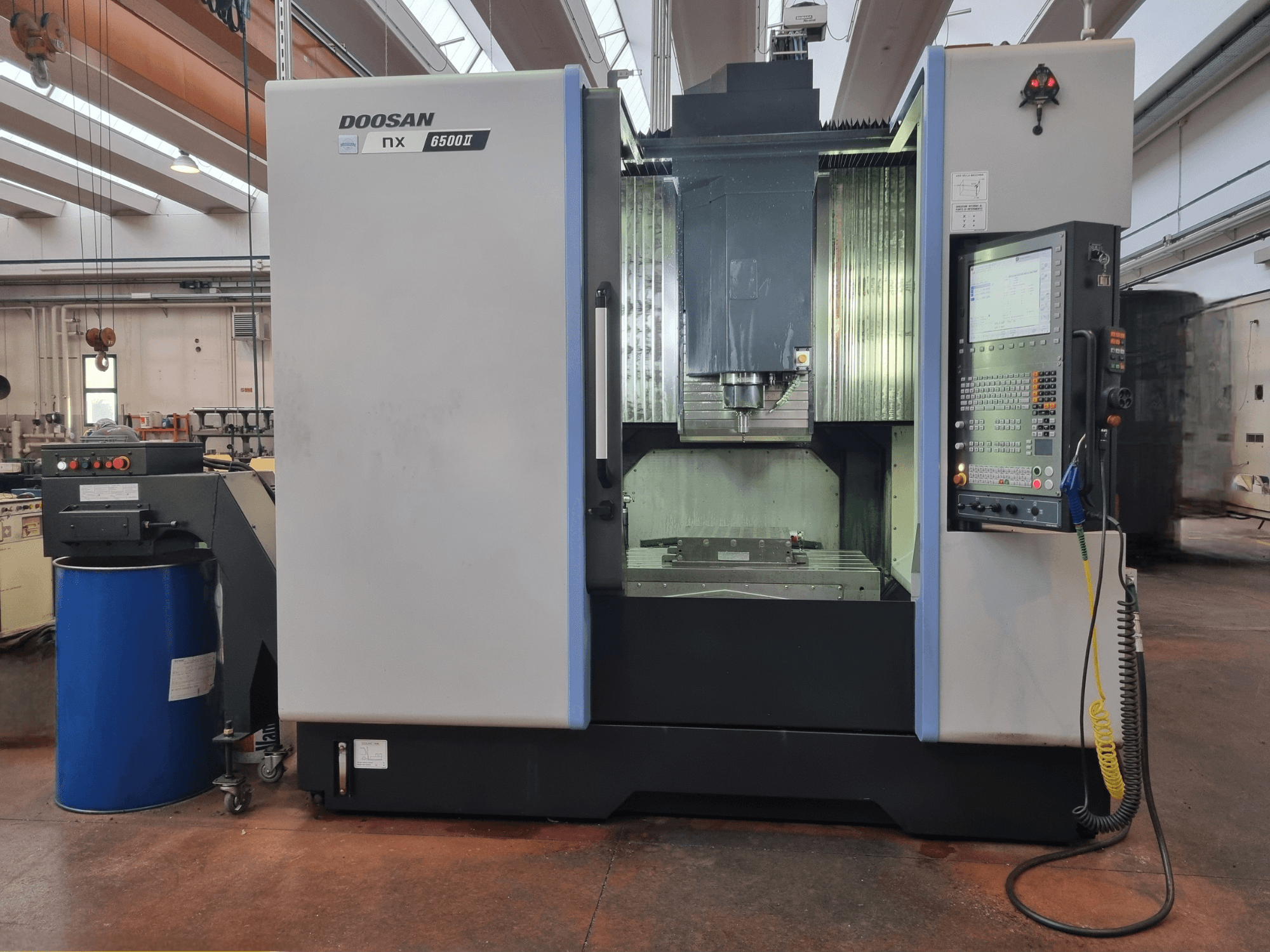 Станок с ЧПУ Doosan NX 6500 II, вид спереди, панель управления и зона обработки, расположенные рядом с синей бочкой.