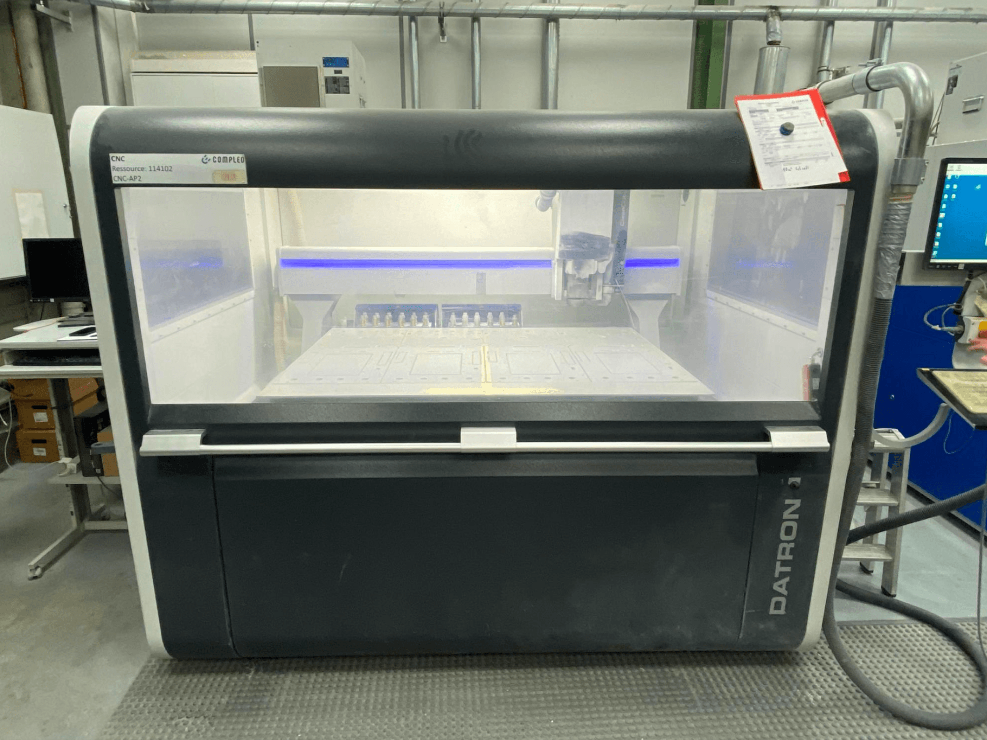 Вид спереди вертикального обрабатывающего центра Datron MLCube B с видимыми элементами управления и рабочим столом в мастерской.