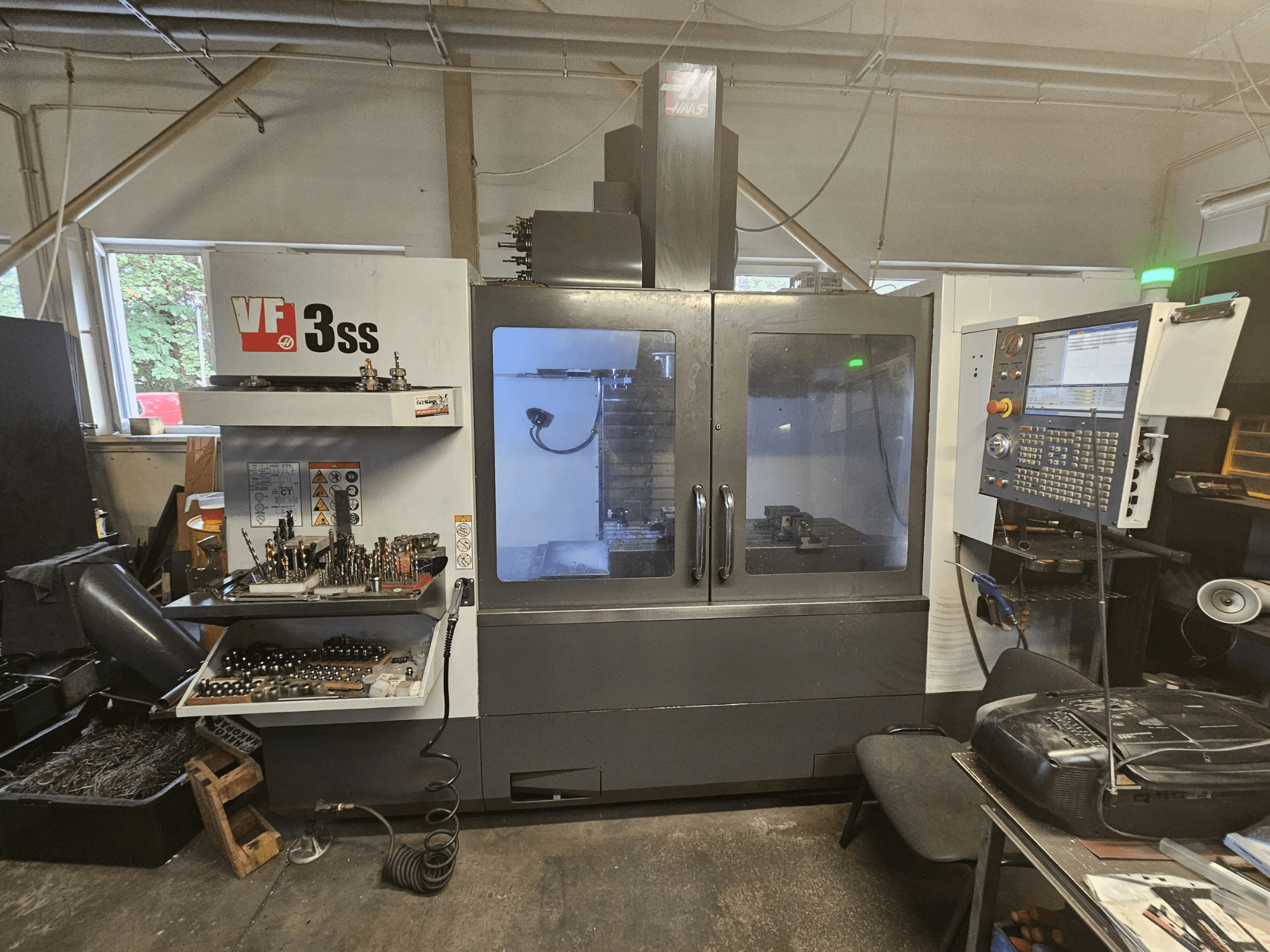 Вертикальный обрабатывающий центр Haas VF-3SS в цехе, вид спереди с панелью управления и отсеком для хранения инструментов.