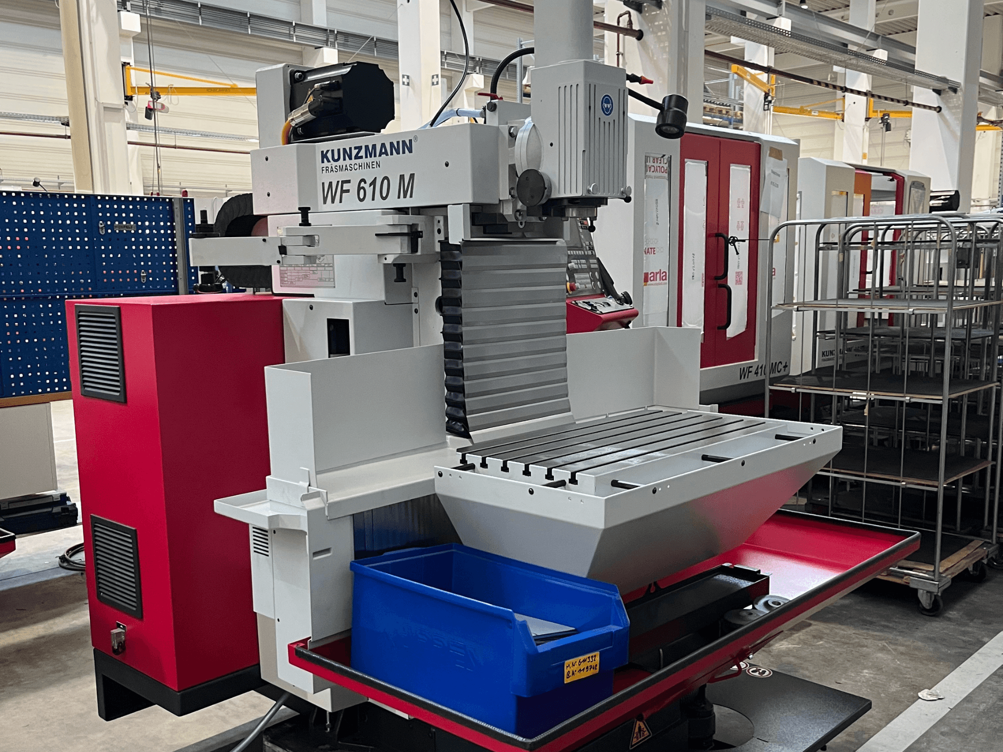 Универсальный обрабатывающий центр KUNZMANN WF 610 M, вид спереди, с держателем инструмента, горизонтальным столом и синим контейнером для хранения.