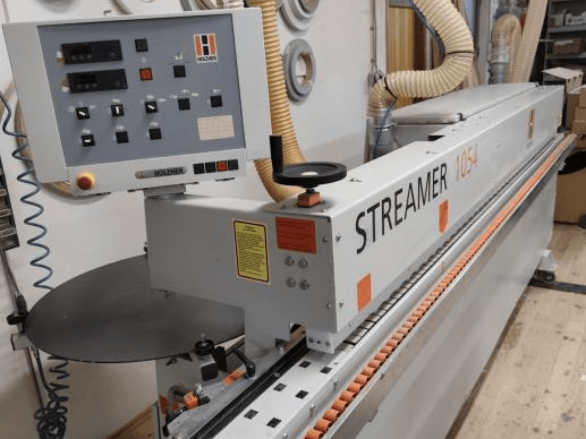 Кромкооблицовочный станок HOLZHER Streamer 1054, вид сбоку, демонстрирующий панель управления и систему подачи на фоне мастерской.