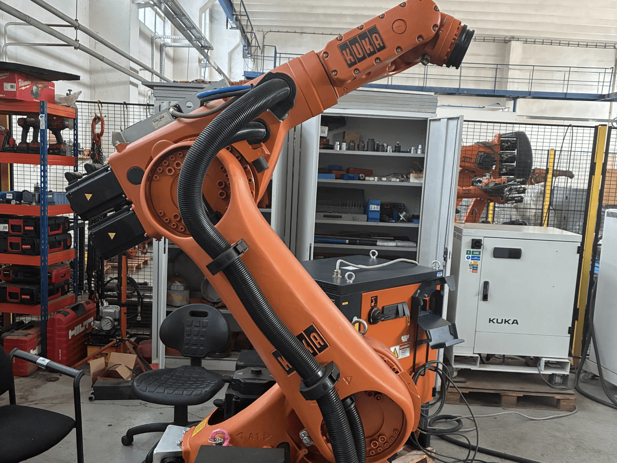 Роботизированная рука KUKA KR30-3 в промышленной обстановке, вид сбоку на кабели и элементы управления, на заднем плане инструменты и стеллажи.