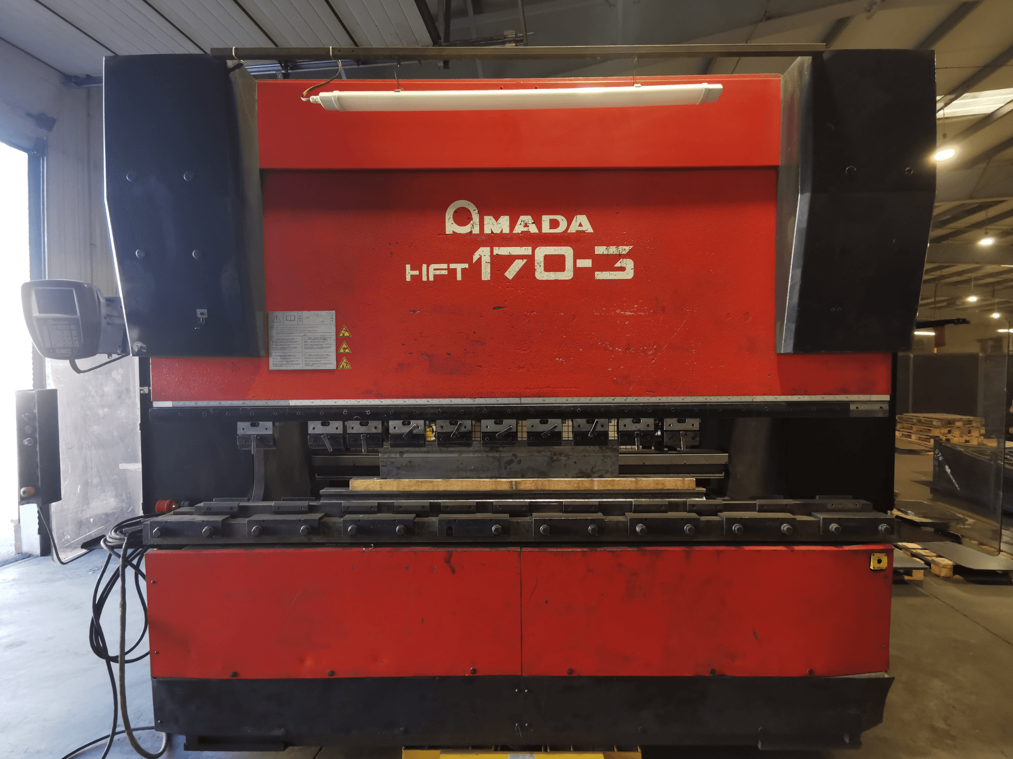 Красный листогибочный станок Amada HFT 170-3 спереди, видна панель управления, гибочные инструменты и рабочая поверхность.