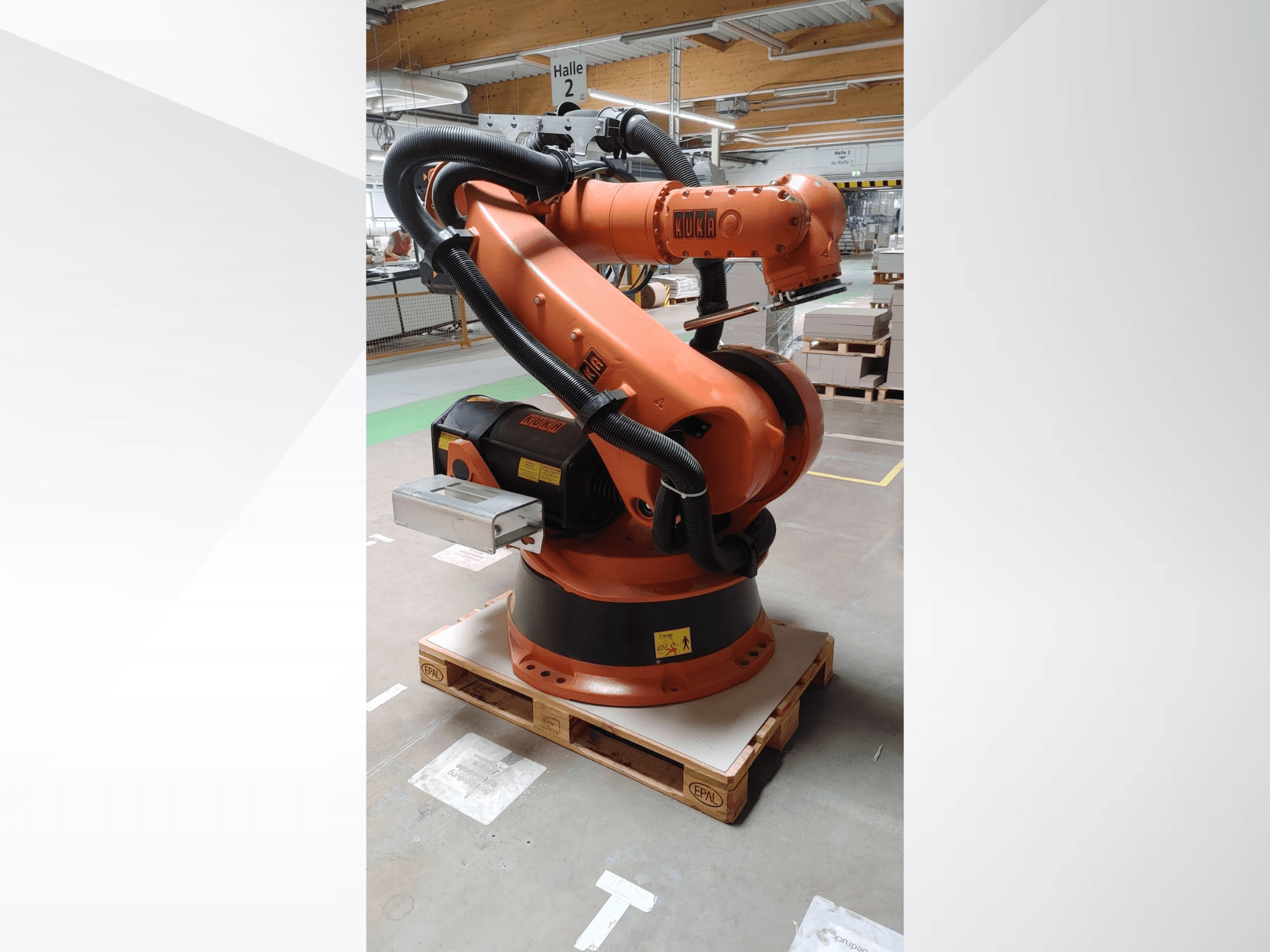 Роботизированная рука KUKA KR140-3 COMP оранжевого цвета, вид спереди на деревянном поддоне, с изогнутой рукой и блоком управления.