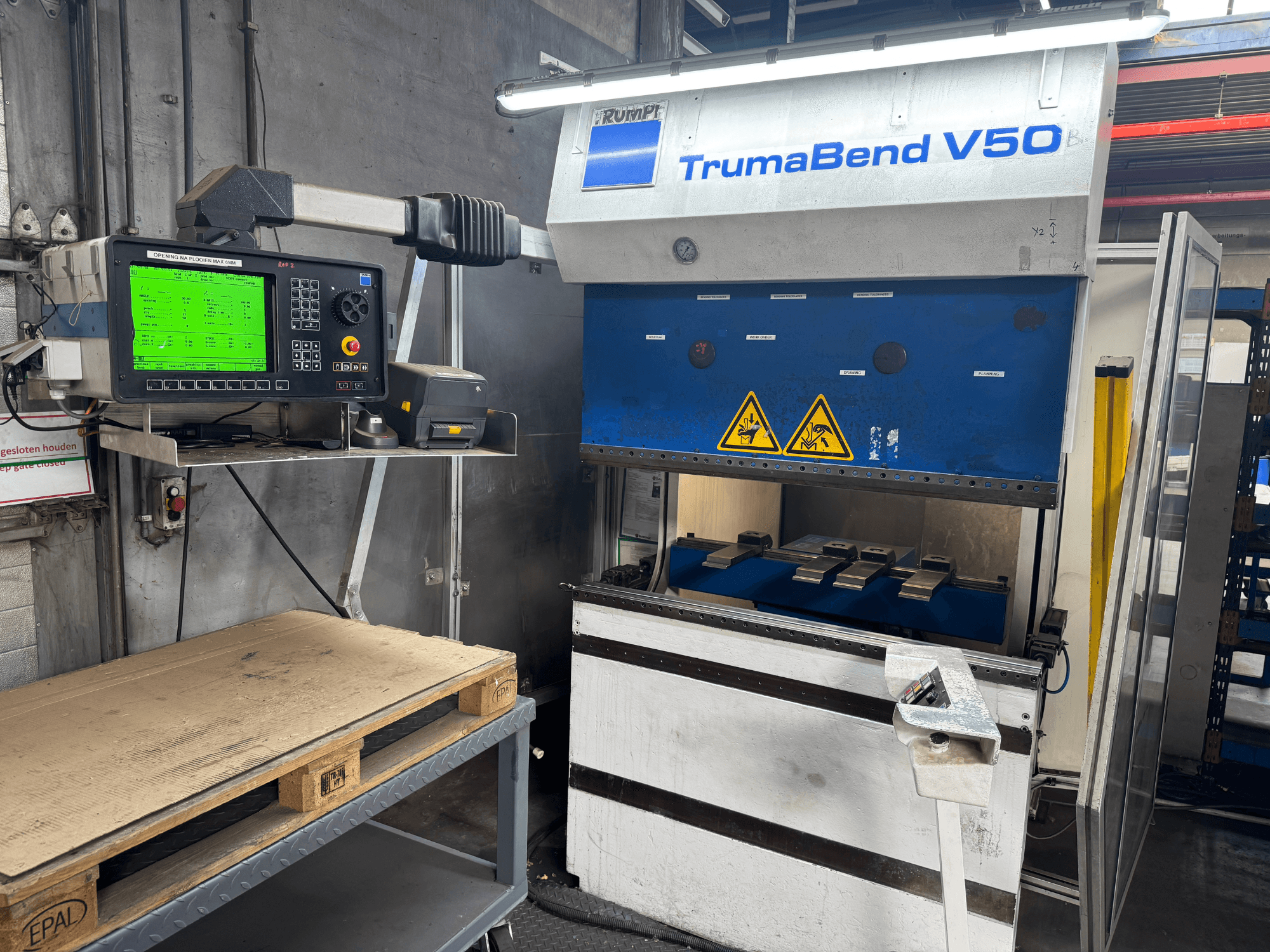 Листогибочный пресс TRUMPF TrumaBend V50, вид спереди, с панелью управления, на которой отображаются настройки и предупреждающие знаки.