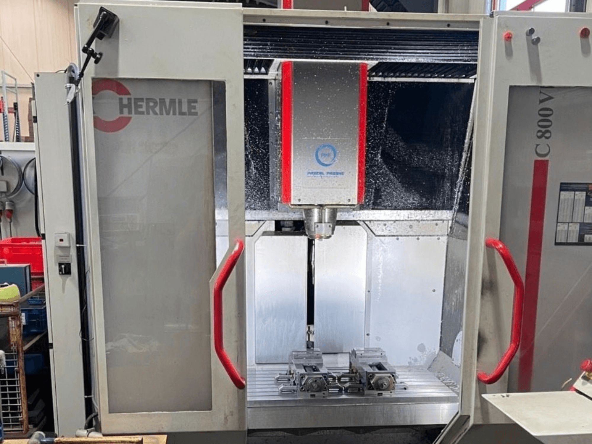 Вертикальный обрабатывающий центр HERMLE C800V, вид спереди, на котором видна зона обработки с заготовками и жидкостной смазкой.