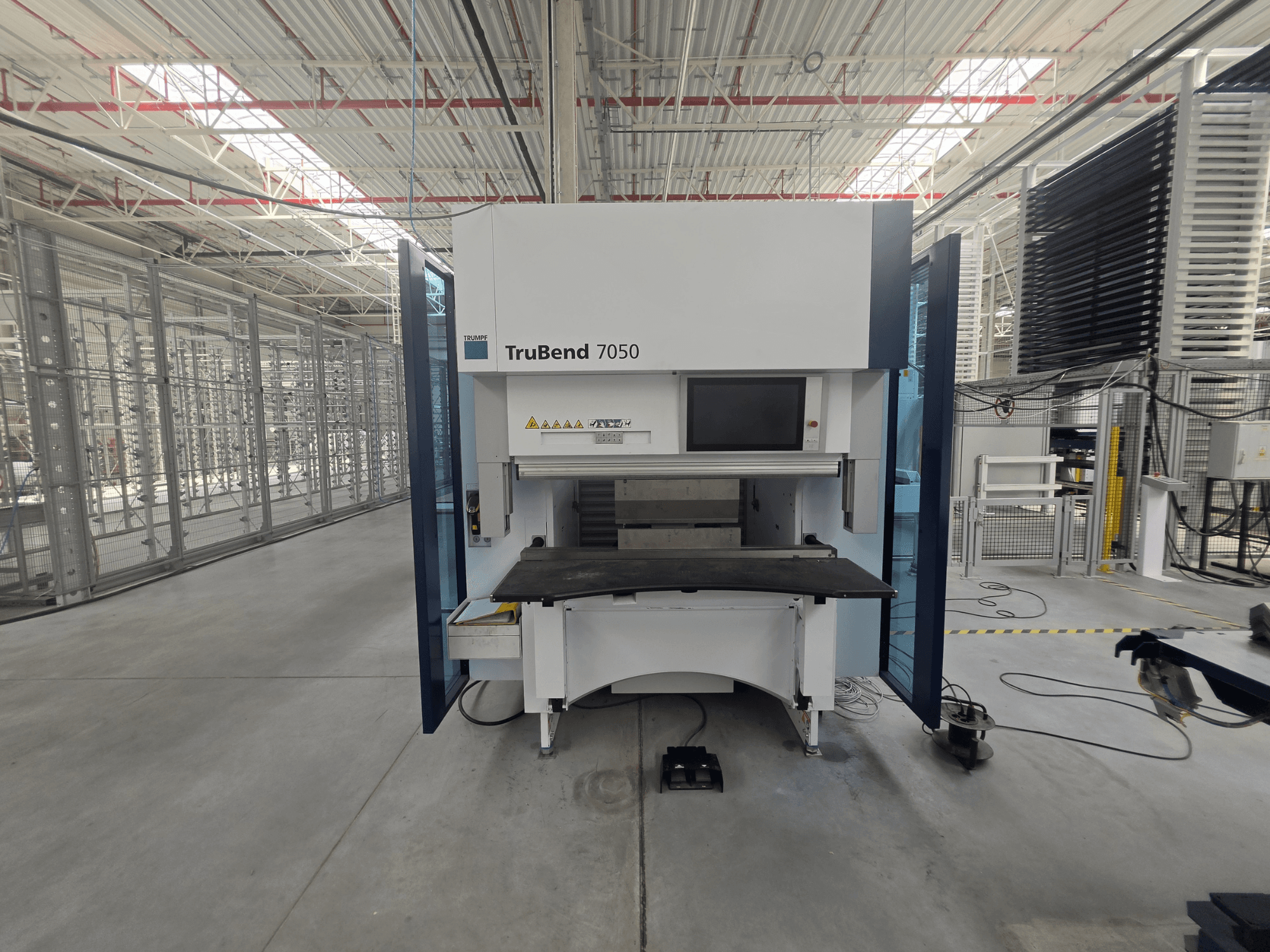 Вид спереди на гибочный пресс TRUMPF TruBend 7050 с панелью управления и рабочим столом в хорошо освещённом промышленном помещении.