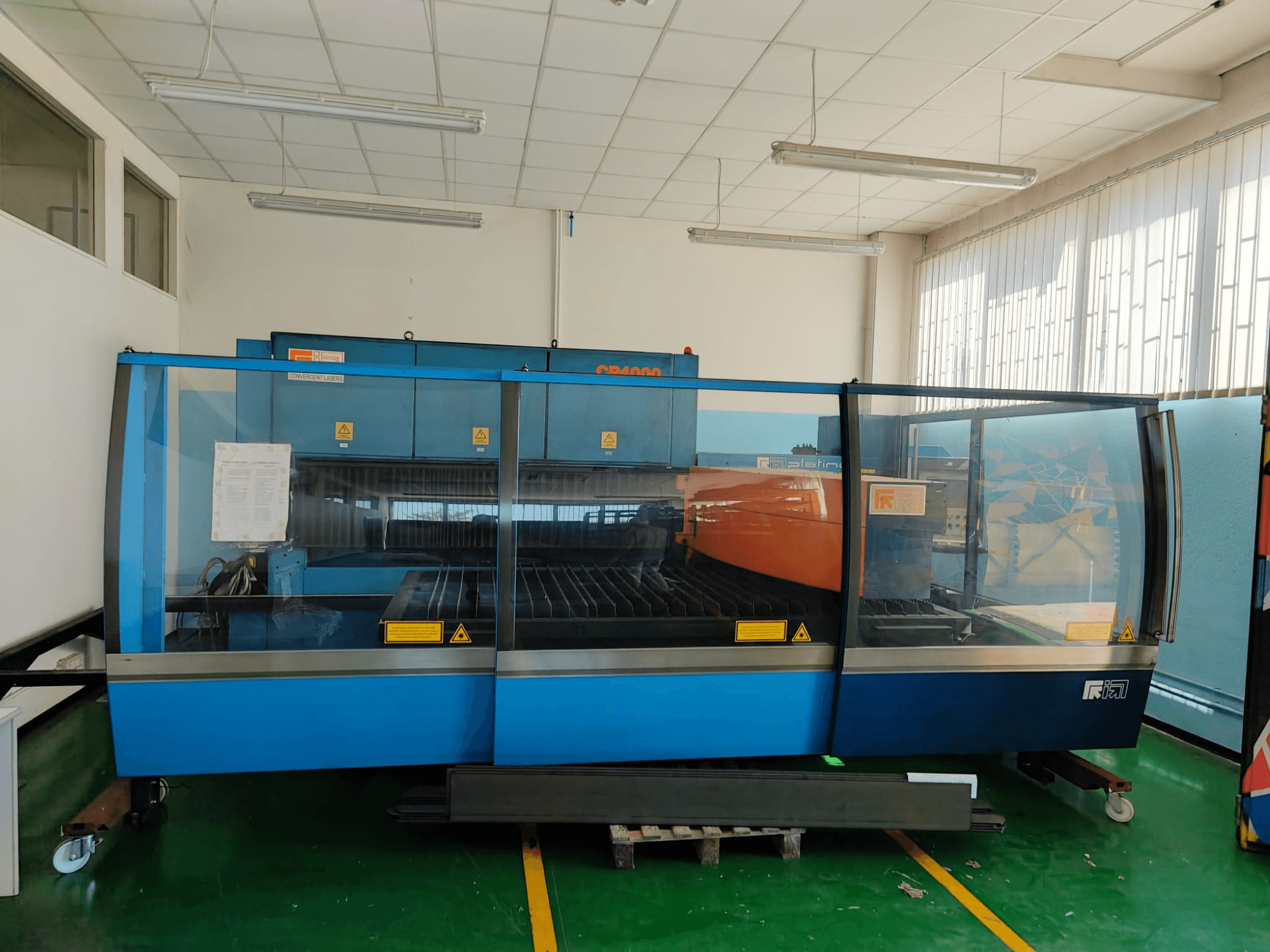 Вид спереди на станок для лазерной резки CONVERGENT LASERS CP4000 с CO2-лазером, оформленный в сине-оранжевых тонах, в хорошо освещённом цехе.