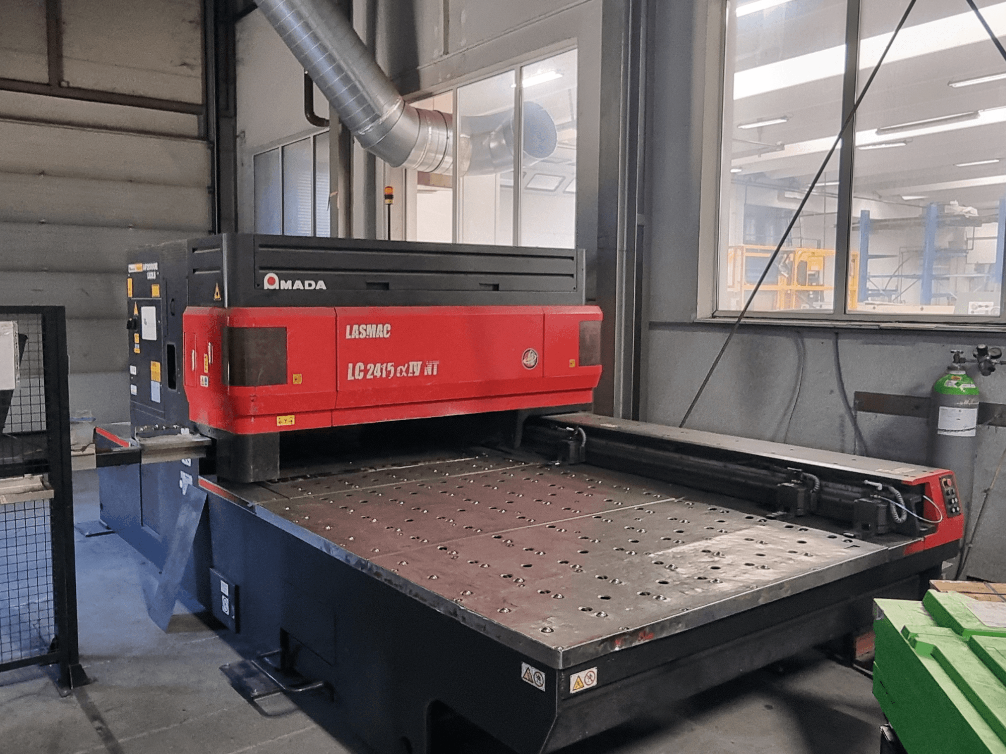 Станок лазерной резки Amada LASMAC LC 2415 αⅡ NT в красно-черном цвете, вид спереди, с приводимой в движение режущей станиной и прецизионными элементами управления.