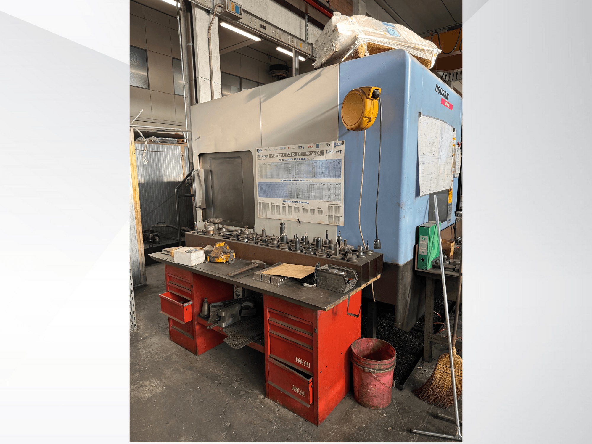 Обрабатывающий центр Doosan с красным верстаком и складом, на котором размещены инструменты и оборудование, вид спереди.