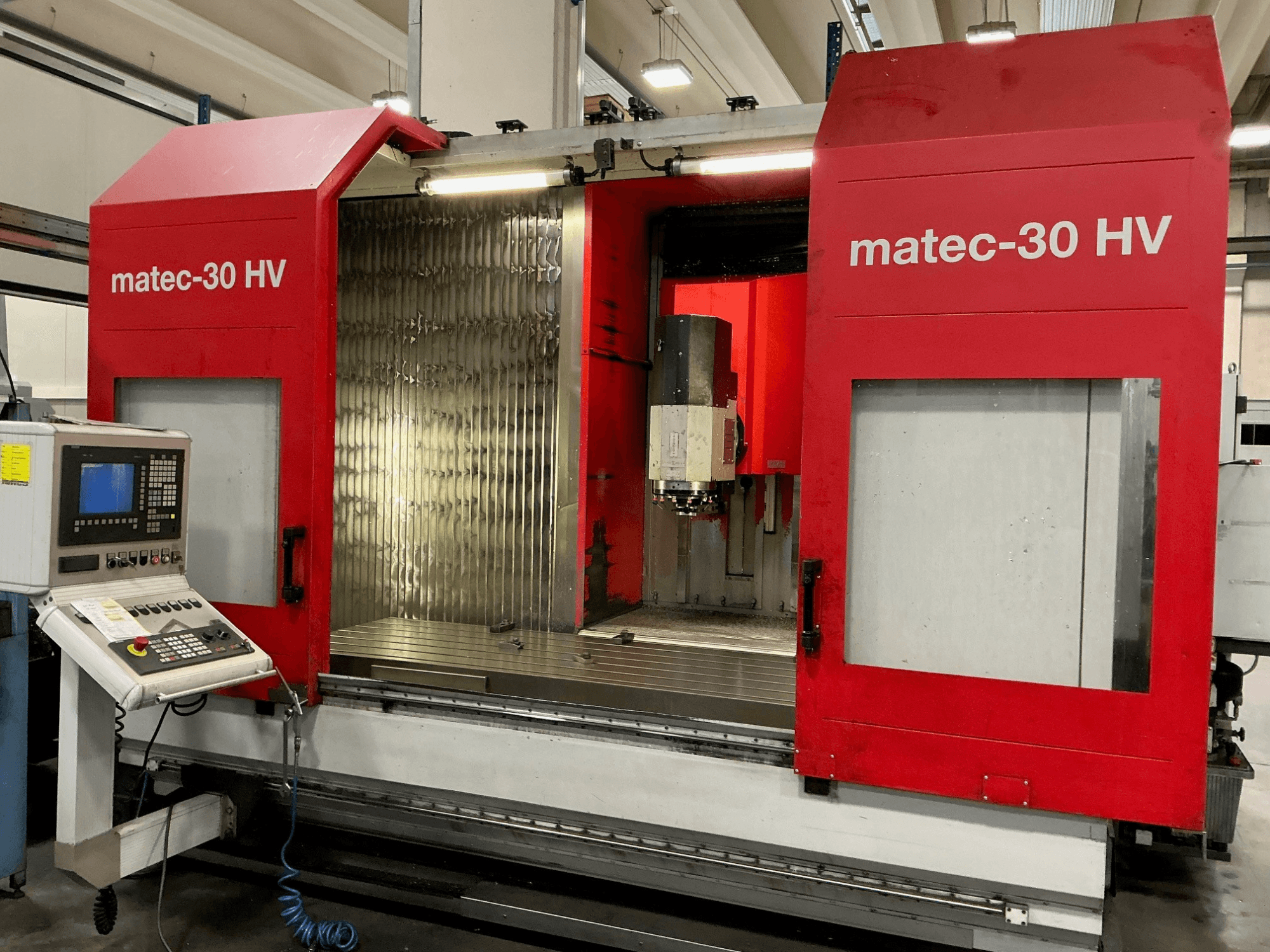 Вертикальный обрабатывающий центр Red Matec 30 HV на переднем плане, панель управления и открытые двери, открывающие зону резки.