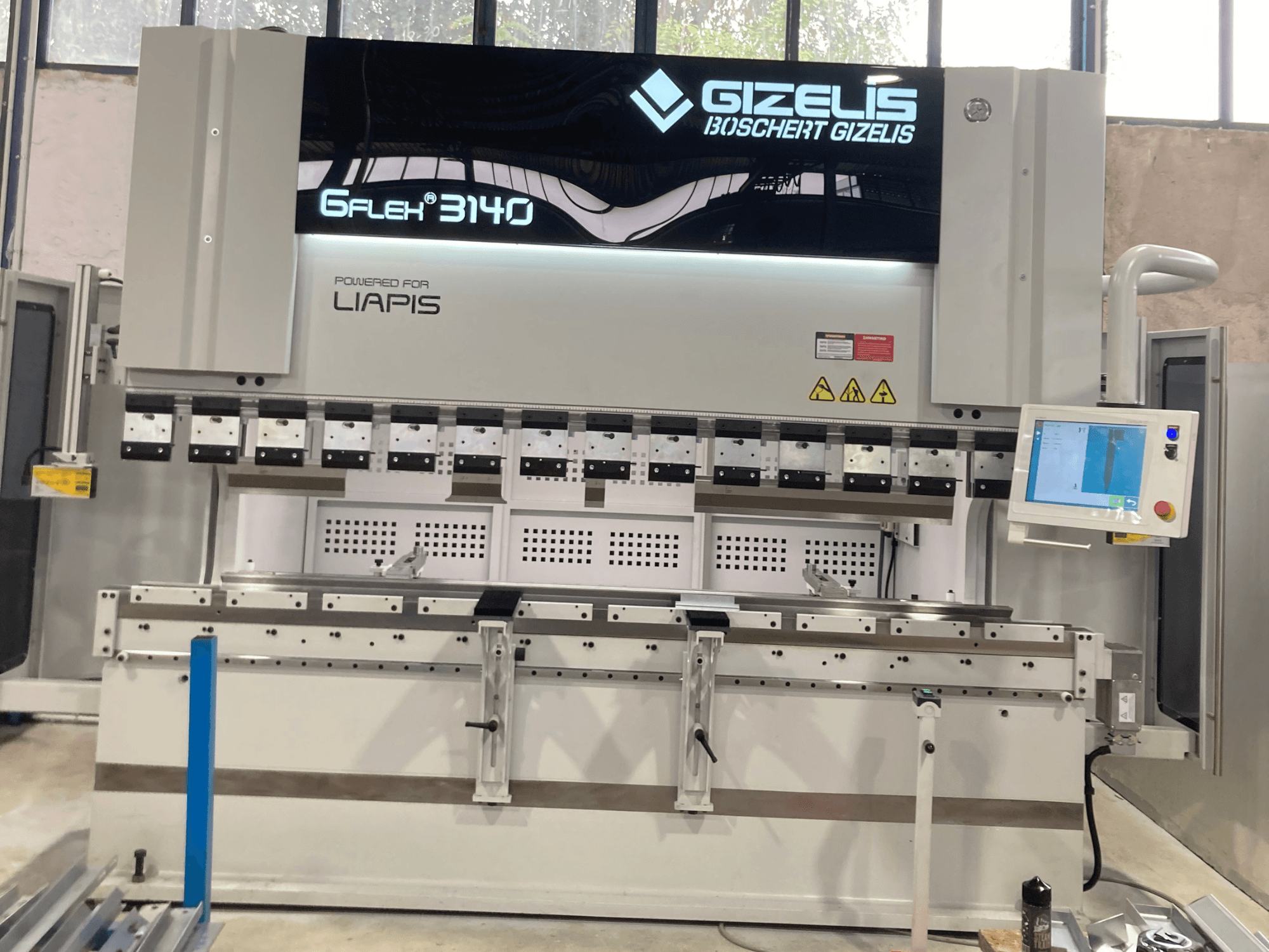 Гидравлический пресс GIZELIS G-FLEX 3140 с видом спереди, с экраном управления, с несколькими гибочными инструментами и наклейками безопасности.