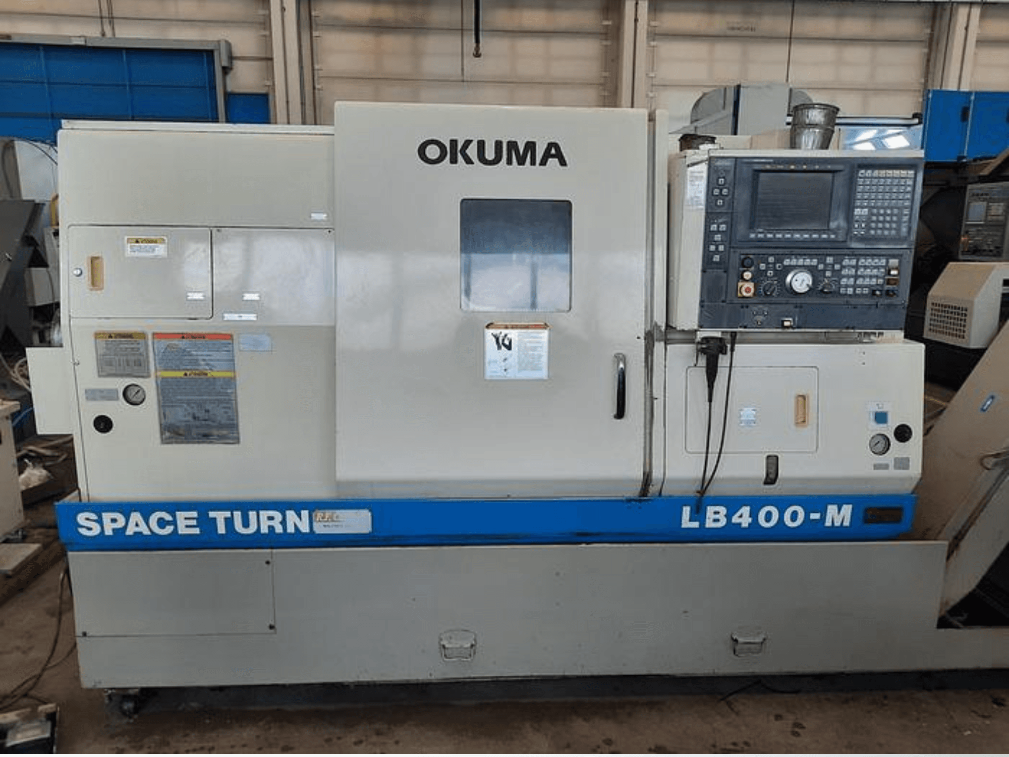 Токарный станок с ЧПУ Okuma LB400-M, вид спереди, видна панель управления, предупреждающие надписи и синяя маркировка "SPACE TURN".