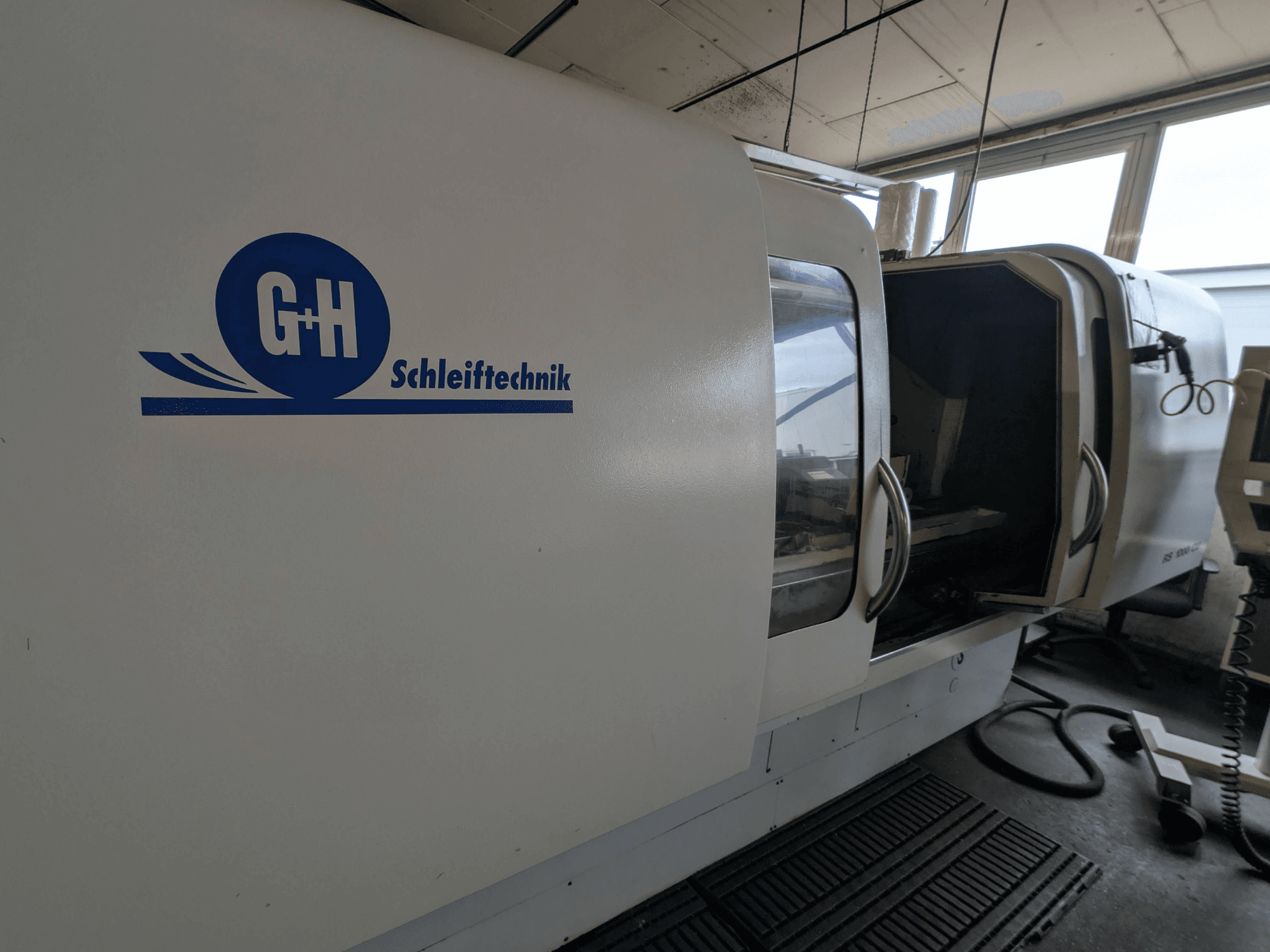 Цилиндрический шлифовальный станок GEIBEL & HOTZ RS 1000 CU, вид сбоку с изображением панели управления и открытой дверцы.