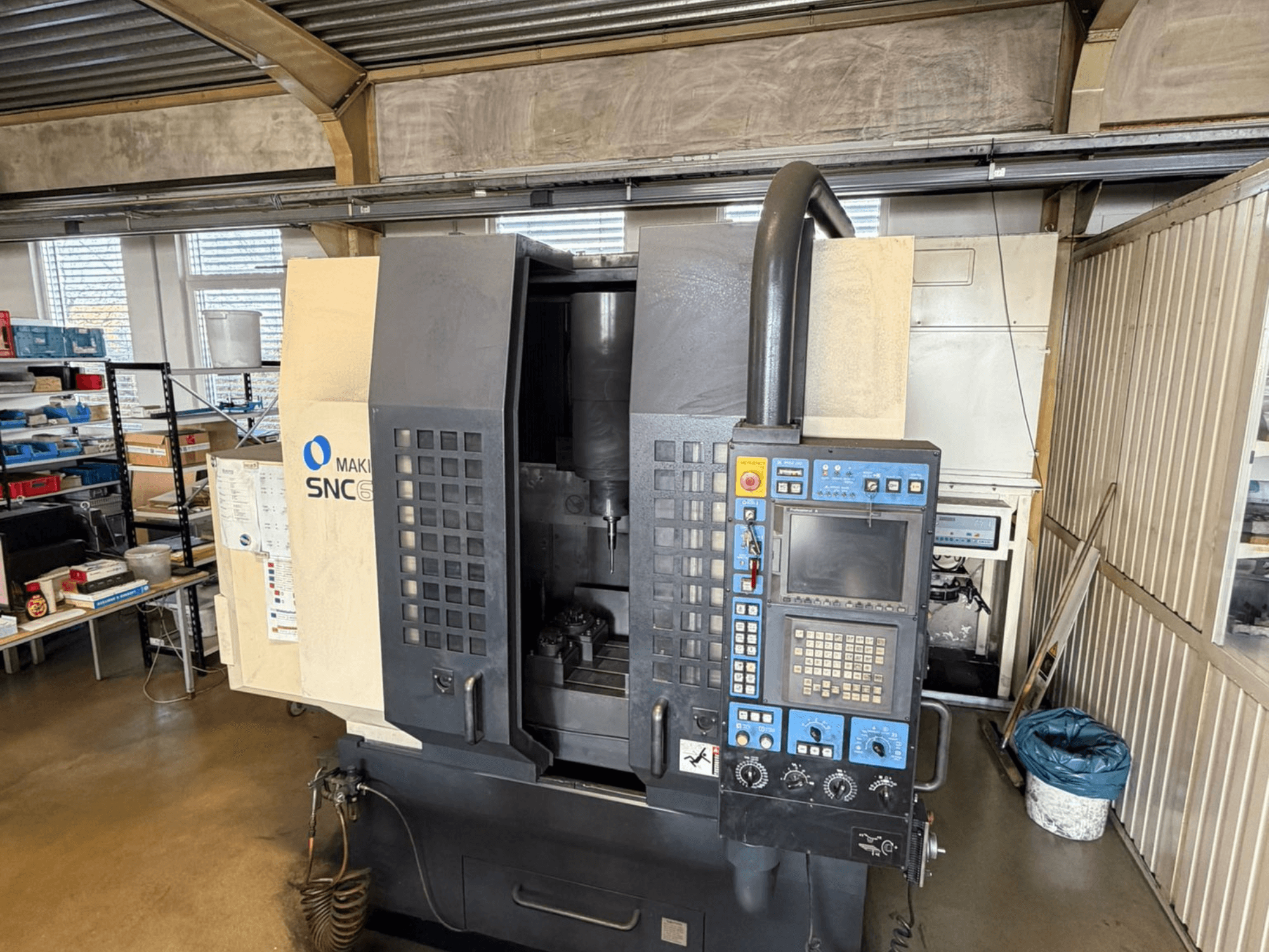 Вертикальный обрабатывающий центр Makino SNC 64-A15 с видом спереди, демонстрирует панель управления, зону обработки и рабочее место.