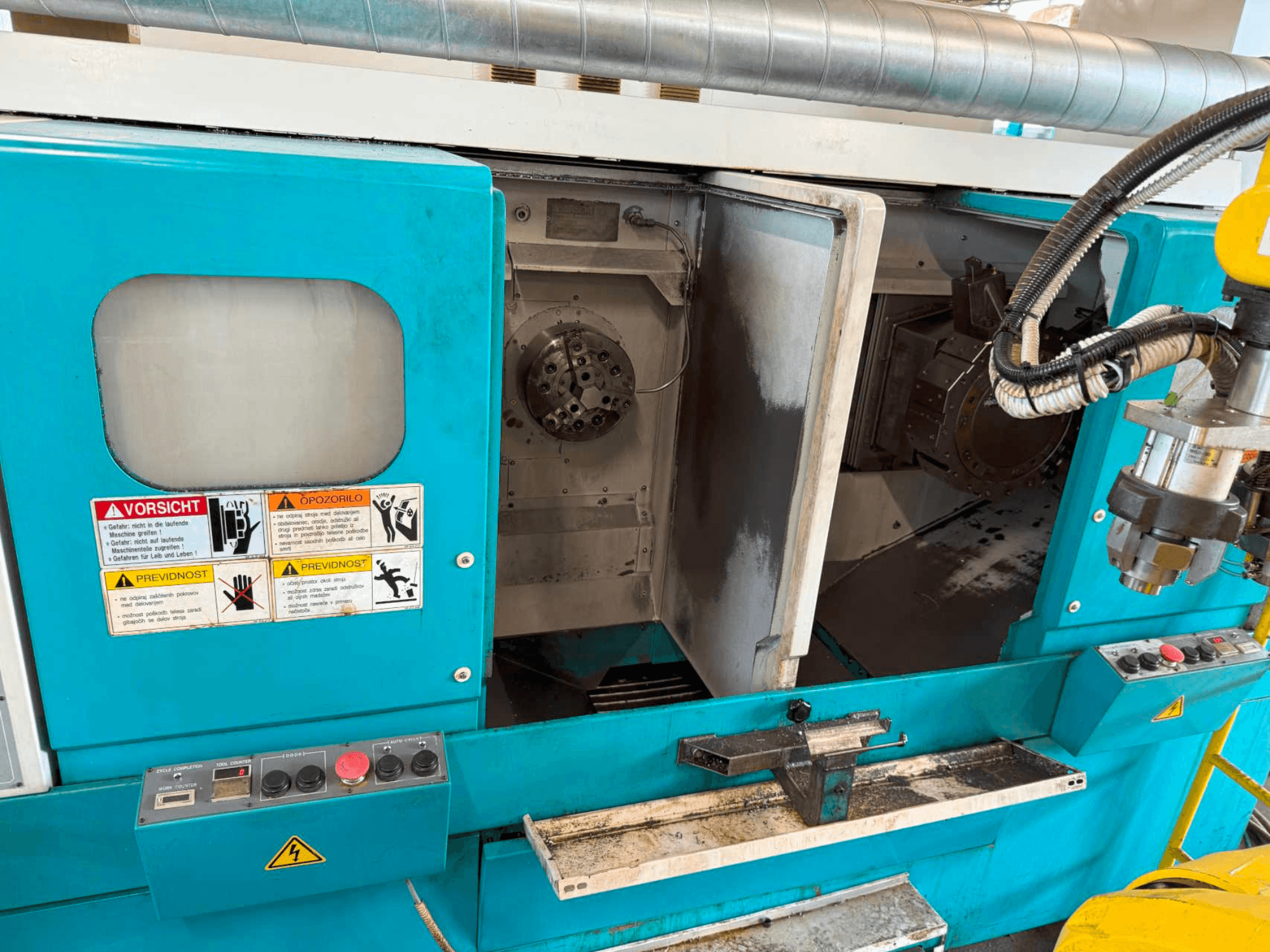 Горизонтальный токарный станок DOOSAN H310T, вид спереди с изображением панели управления и зоны шпинделя с предупреждениями о безопасности.