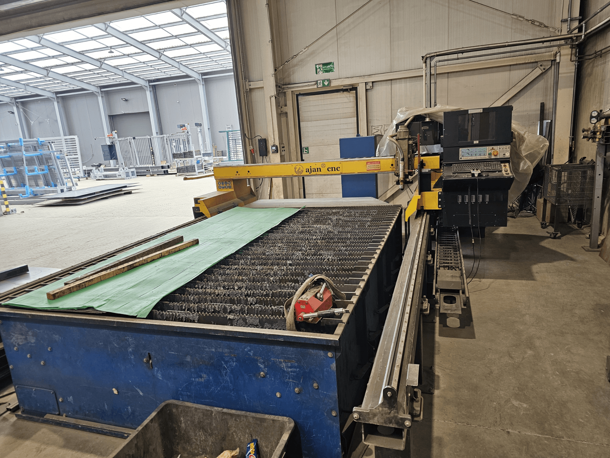 Машина плазменной резки AJAN PP16011 с видом сбоку, со столом для резки и панелью управления, установленная в мастерской.