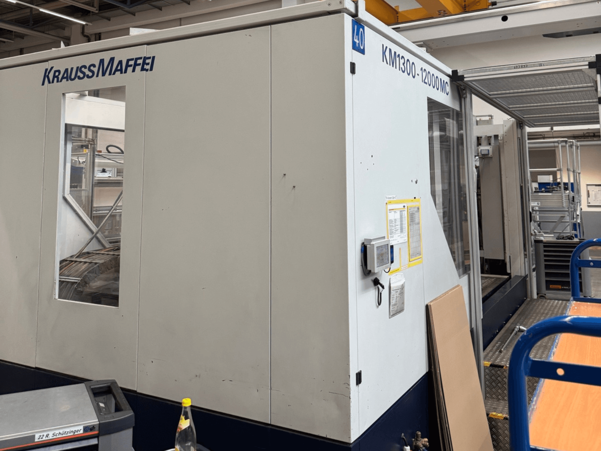 Гидравлическая машина для литья под давлением Krauss Maffei KM1300-12000 MC, вид сбоку, демонстрирует панель управления и рабочее пространство.