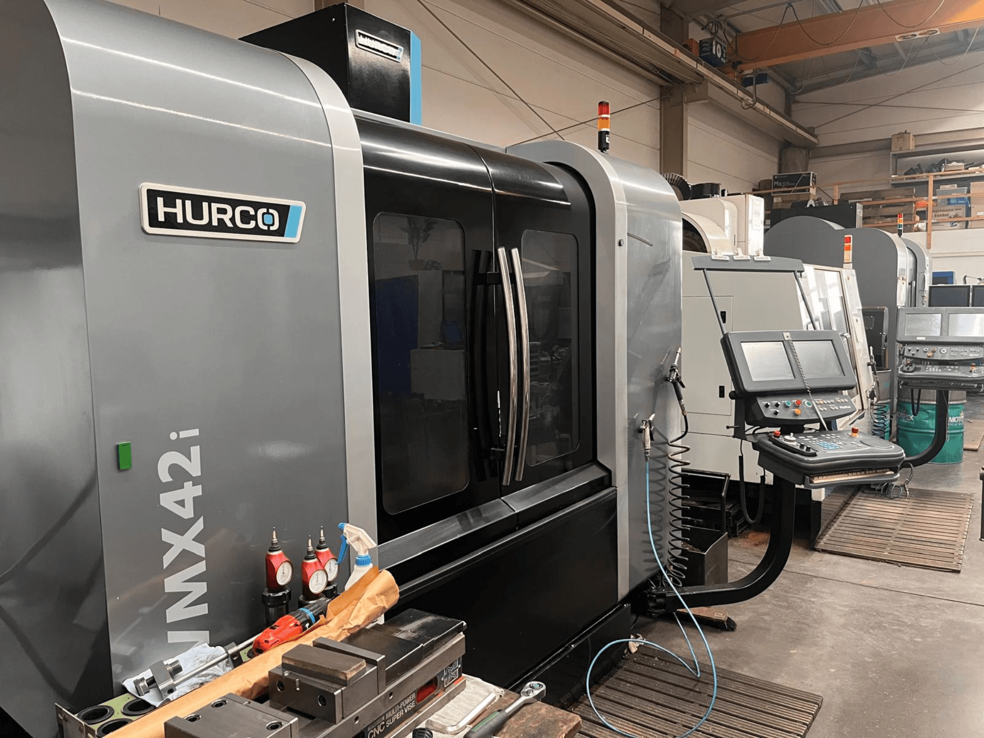 Станок с ЧПУ Hurco VMX42i в мастерской, вид спереди, панель управления и различные инструменты на верстаке.
