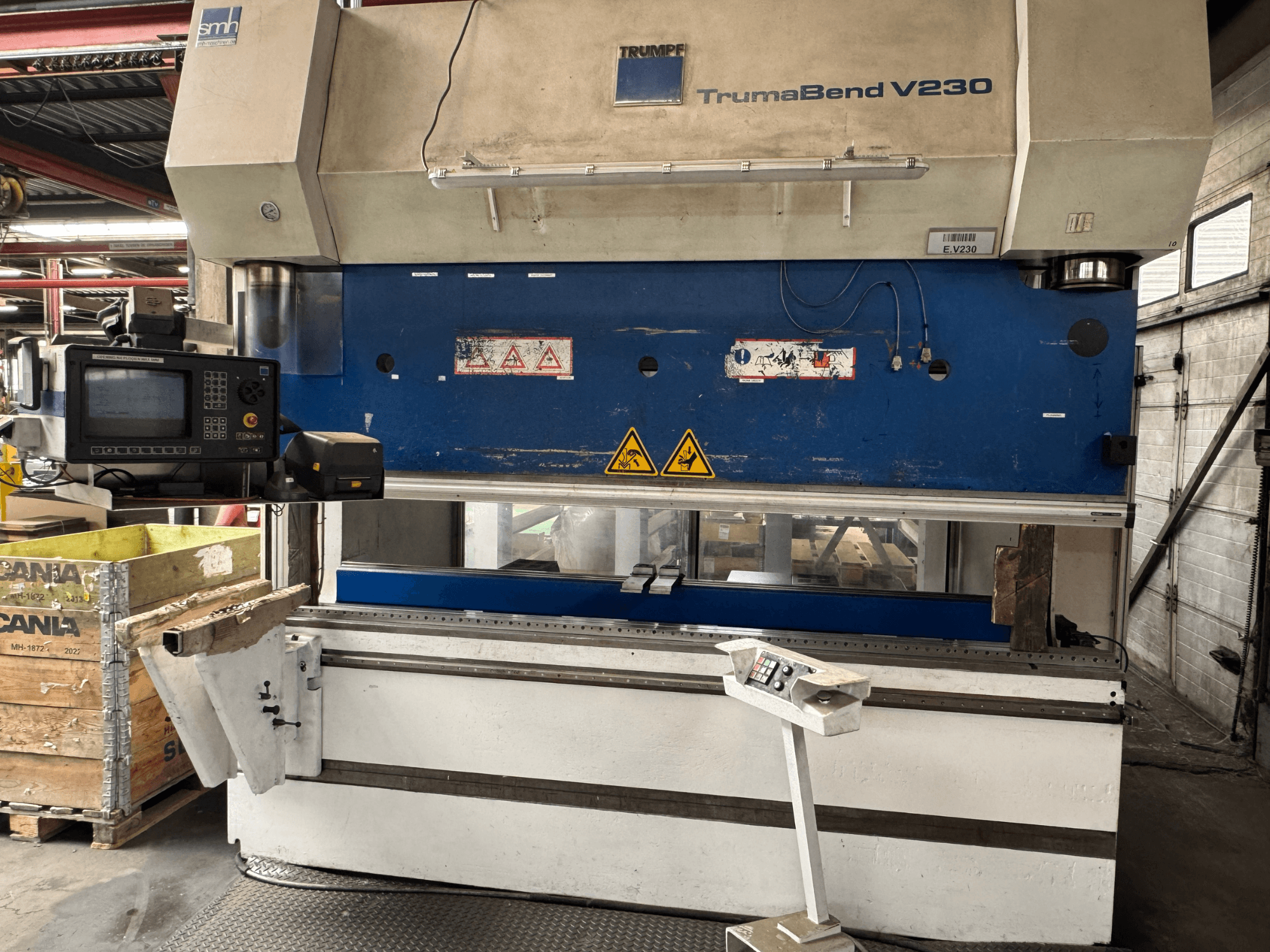 Листогибочный станок TRUMPF TrumaBend V230, вид спереди, видны панель управления, предупреждающие надписи и рычаг для поддержки заготовки.
