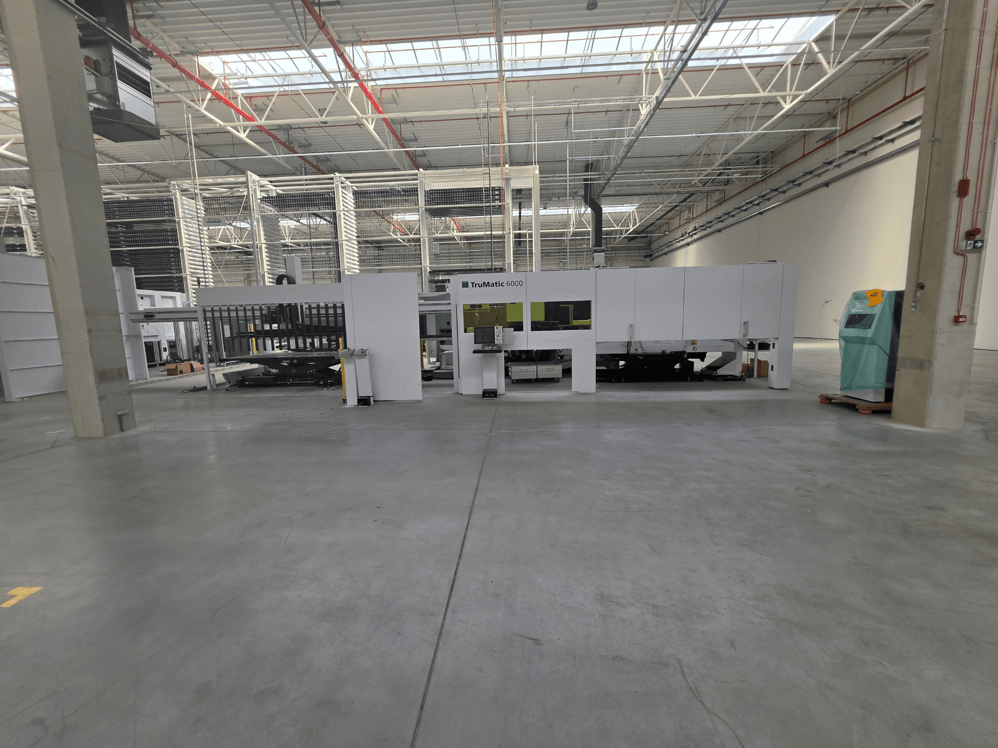 Комбинированный станок TRUMPF TruMatic 6000-1600 с волоконно-оптическим лазером и штамповочным механизмом в просторном складе, вид спереди.