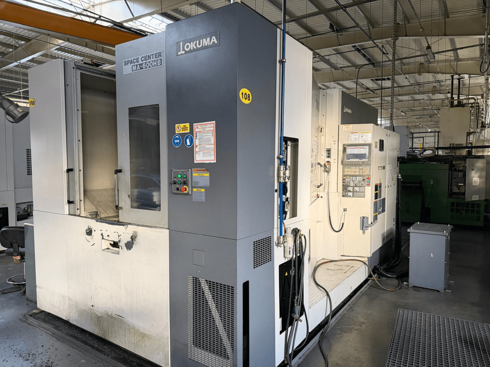 Горизонтальный обрабатывающий центр Okuma MA-600 HB, вид спереди, демонстрирует панель управления и зону резания с видимыми следами износа.