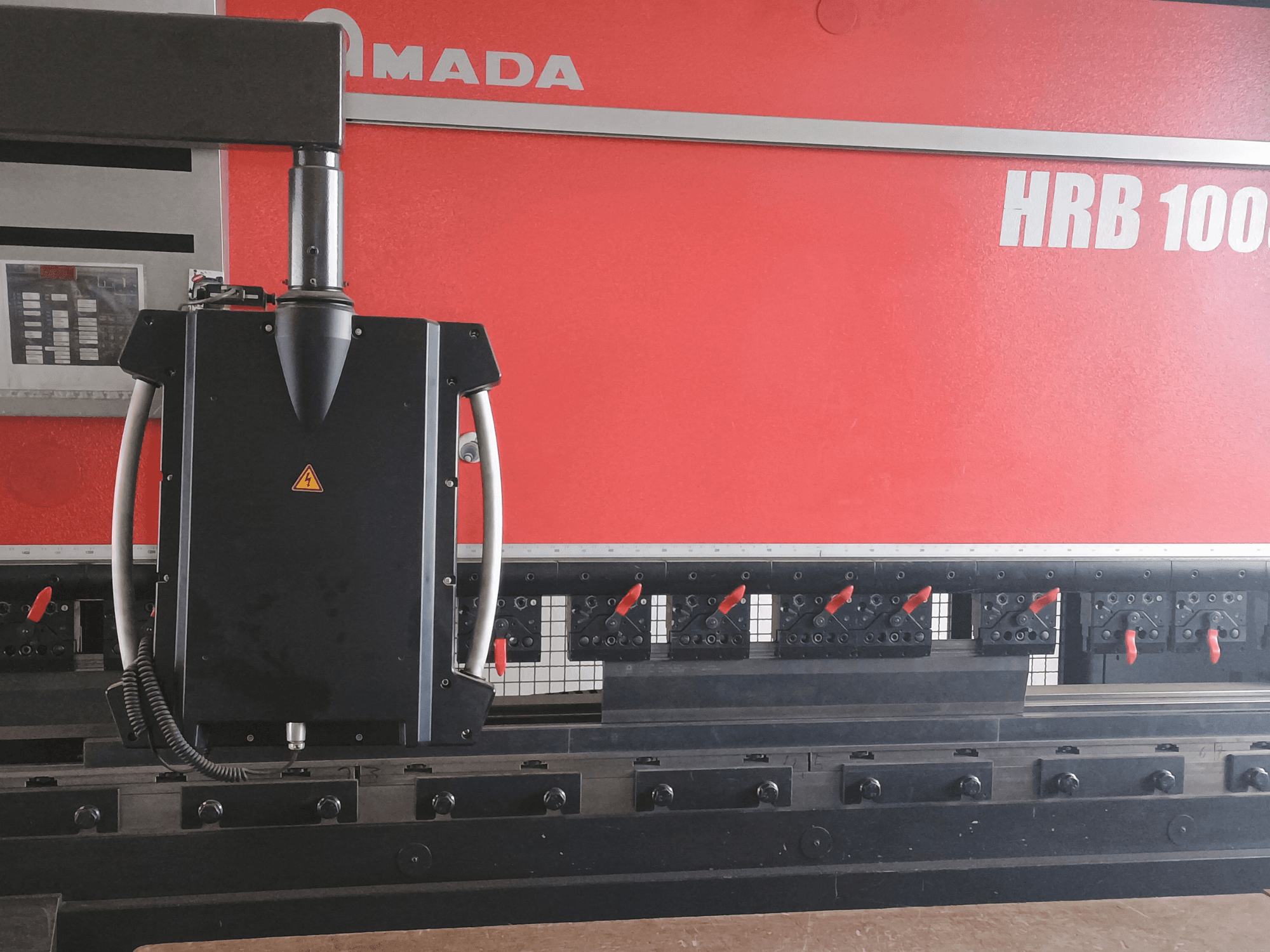 Гибочный станок Amada HRB 100 вид спереди; имеет черную головку управления с коническим соплом и регулируемыми зажимами.