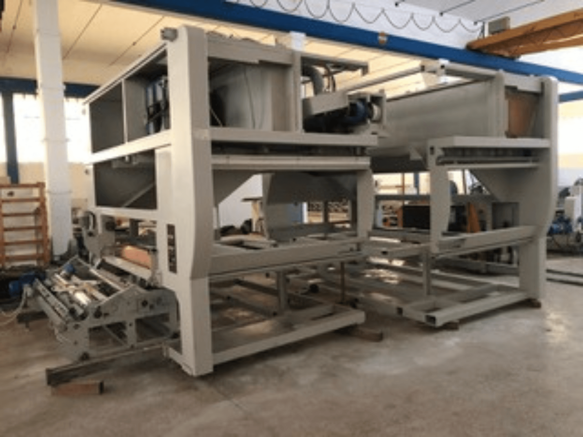 Промышленная машина с несколькими конвейерными роликами и большой конструкцией; вид сбоку, цвет серый, расположена на хорошо освещенной фабрике.