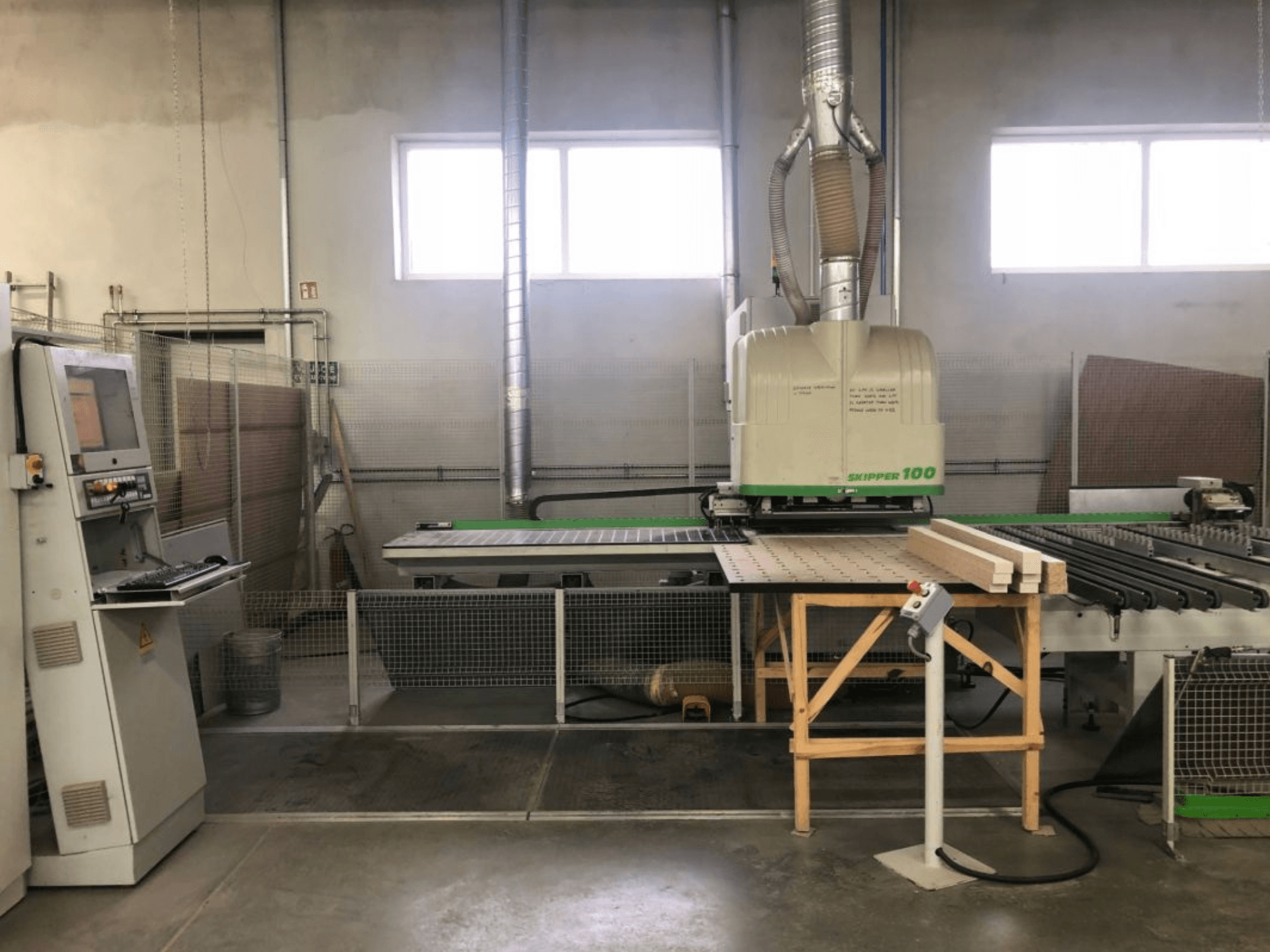 Обрабатывающий центр BIESSE SKIPPER 100 с ЧПУ в цехе; на фотографии, сделанной с передней стороны, виден станок с панелью управления и заготовкой на столе.