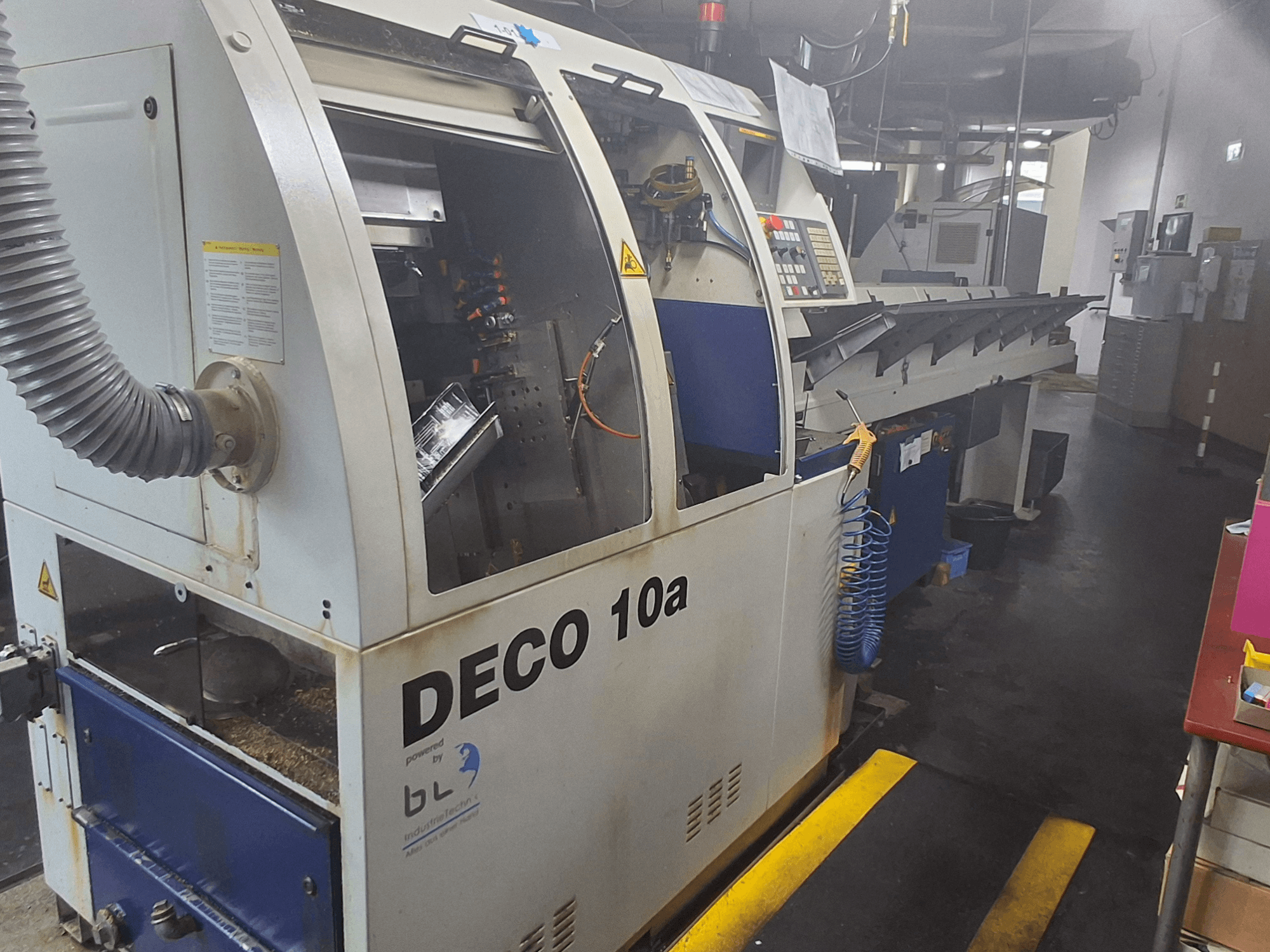 Токарный станок швейцарского типа TORNOS DECO 10a, вид спереди; имеет панель управления, видимые механизмы и трубку для удаления пыли.