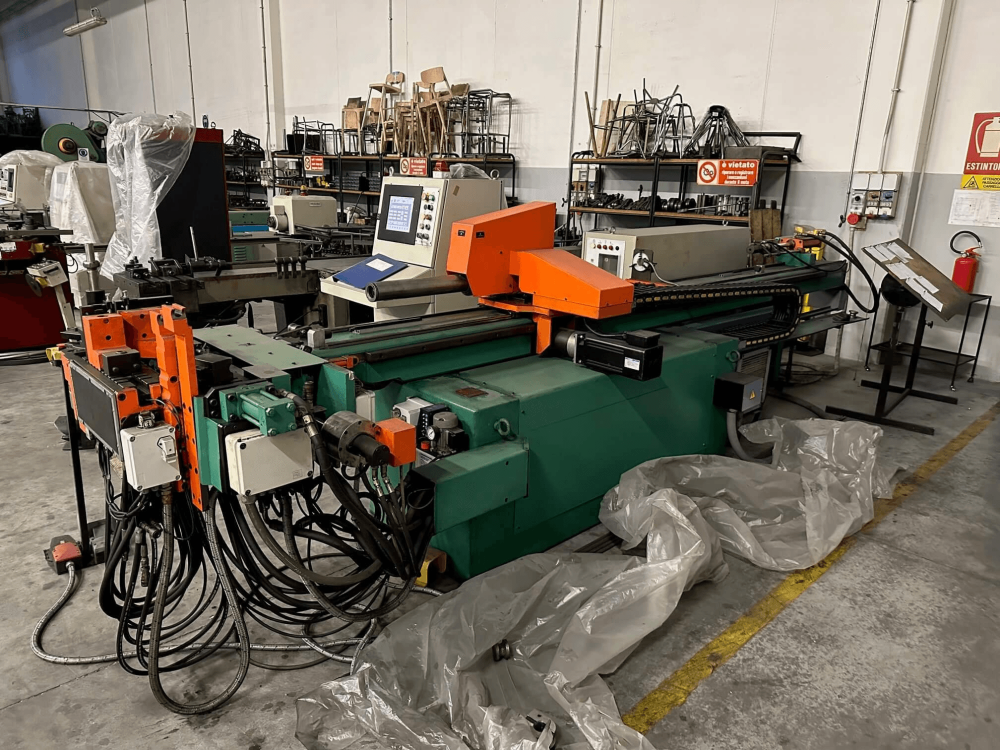 Промышленный станок с оранжево-зеленым корпусом, панелью управления и многочисленными кабелями, вид спереди в мастерской.