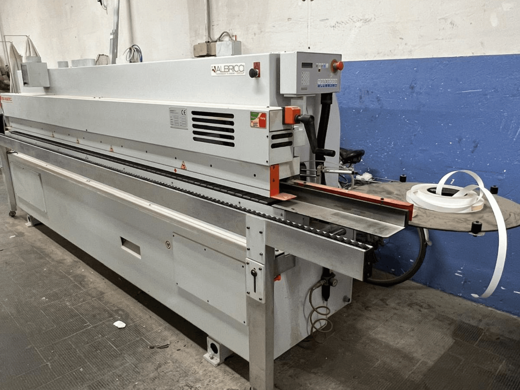 Кромкооблицовочный станок ALBRICO с видом спереди, с длинной конвейерной лентой и прикрепленным рулоном клейкой ленты.