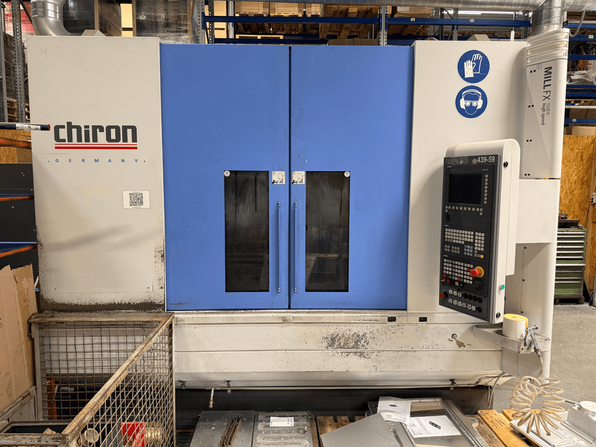 Вертикальный обрабатывающий центр CHIRON MILL FX 1250, вид спереди, с панелью управления и знаками безопасности, готовый к выполнению прецизионных работ.