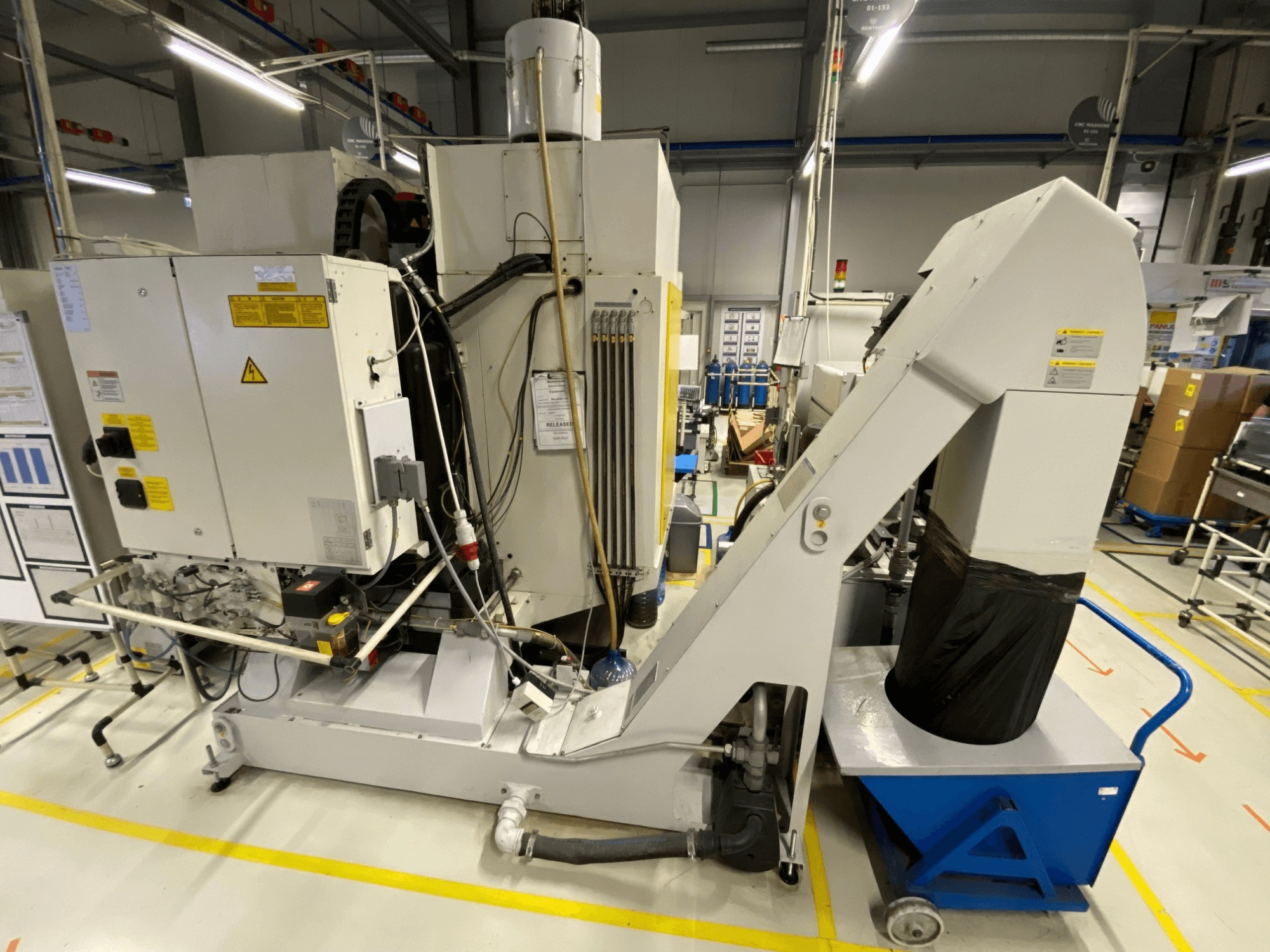Вертикальный обрабатывающий центр FANUC ROBODRILL α-D21LiB, вид спереди, на котором видны электрические компоненты и желоб для выхода заготовок.