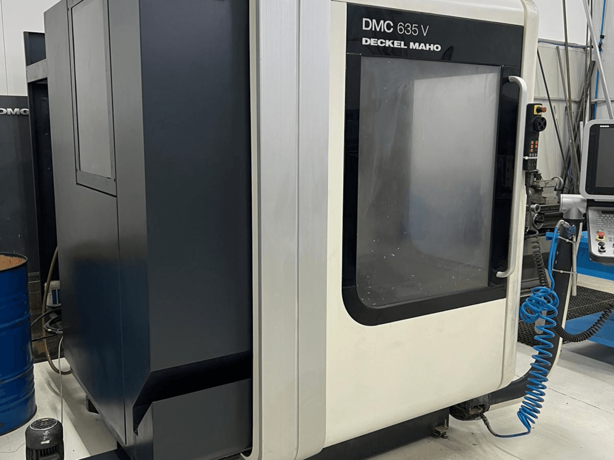 Фрезерный станок DMC 635 V производства Deckel Maho, вид сбоку с изображением панели управления и частично открытой дверцы доступа.