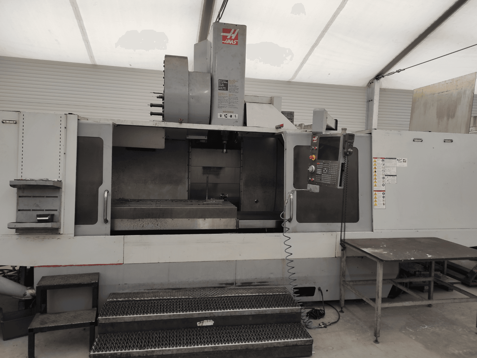 Вертикальный обрабатывающий центр HAAS VF-10/50HE, вид спереди, на котором видны панель управления, станина станка и доступная ступенька для работы.