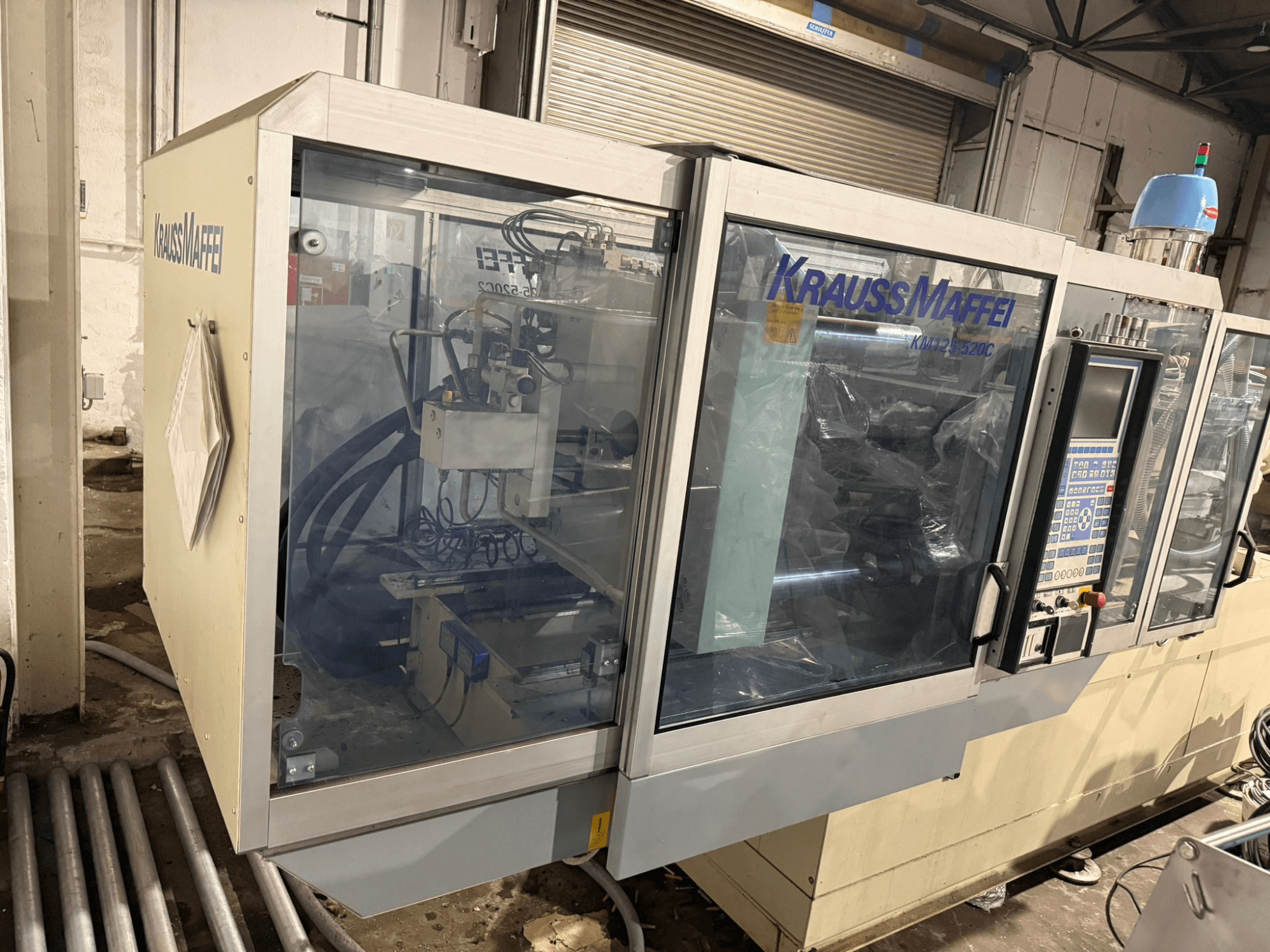 Гидравлическая машина для литья под давлением Krauss Maffei KM125-520C2, вид спереди с панелью управления и прозрачным корпусом.