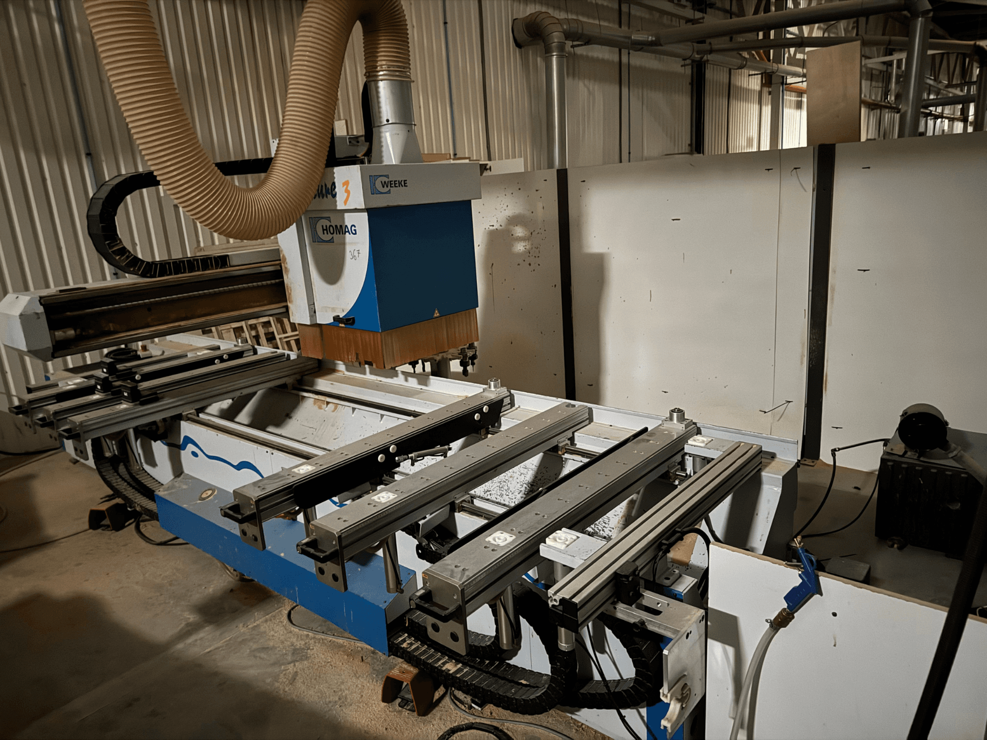 Станок с ЧПУ HOMAG с сине-белым дизайном, вид сбоку, оснащен подвижными направляющими, системой пылеудаления и установленными инструментами.