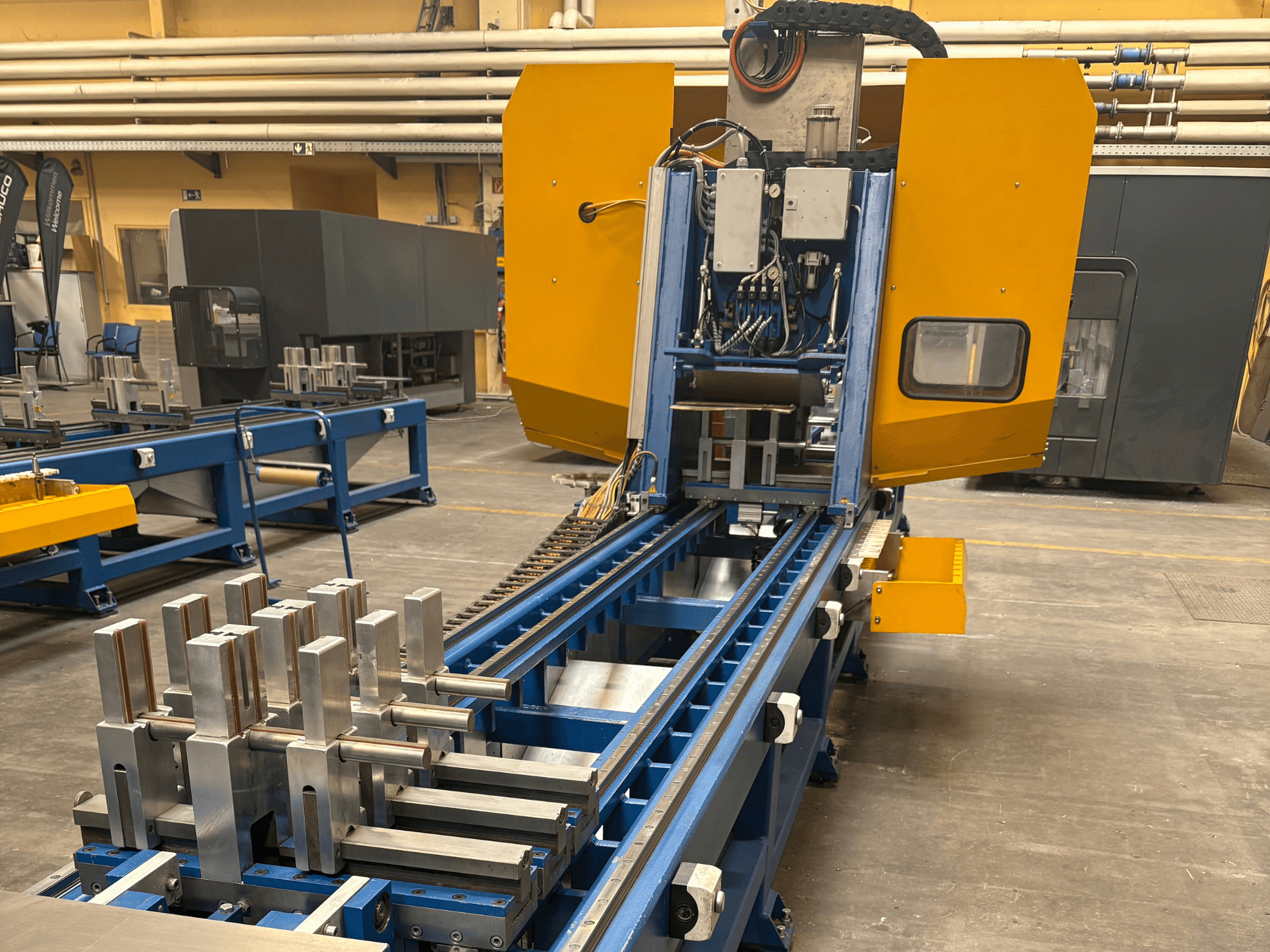 Вид спереди на универсальный обрабатывающий центр SCHÜCO PBX AL, демонстрирующий металлические заготовки на синей обрабатывающей станине.