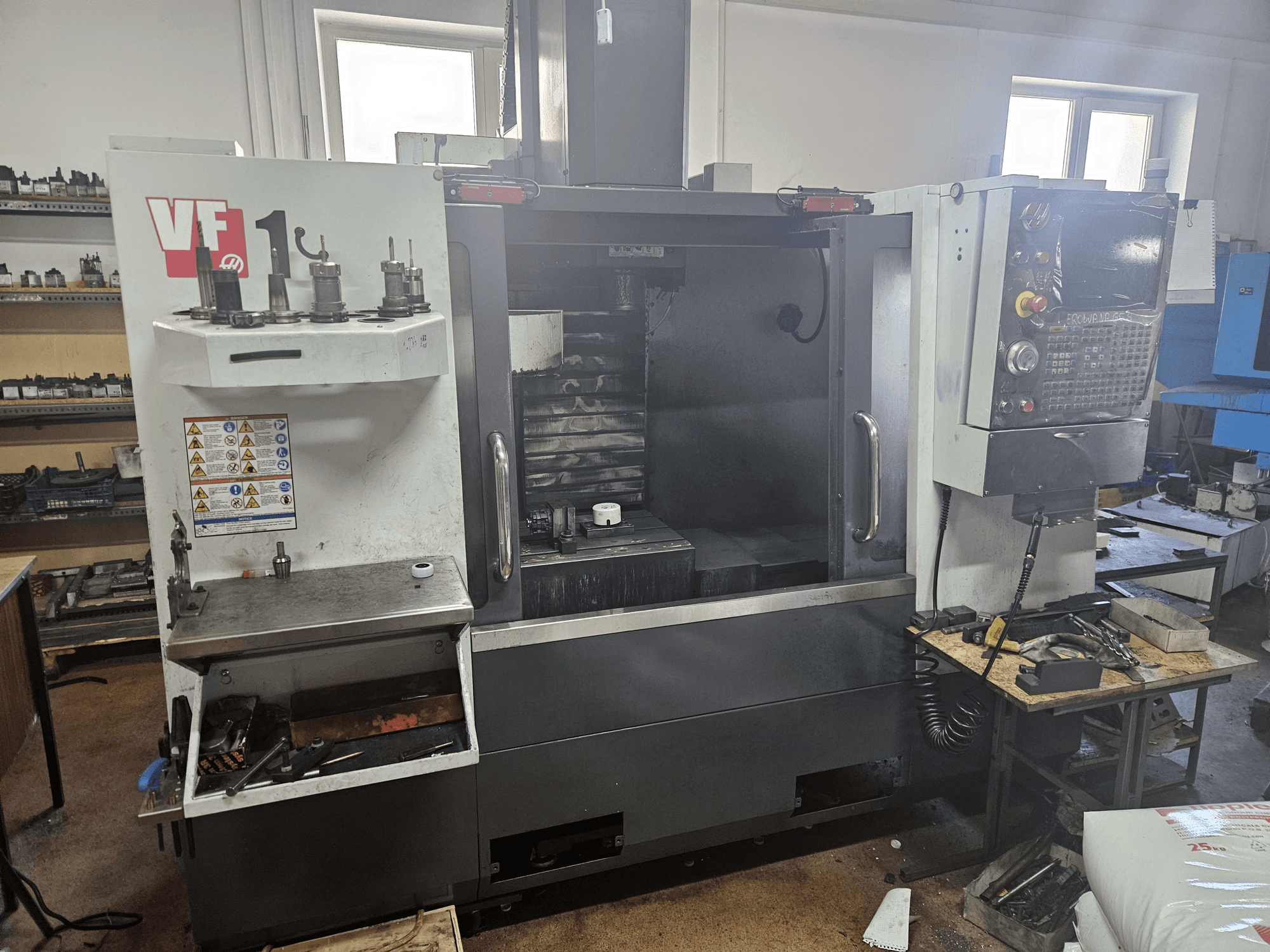 Вертикальный обрабатывающий центр HAAS VF-1, вид спереди с инструментами сбоку, видна панель управления, рабочая зона на заднем плане.