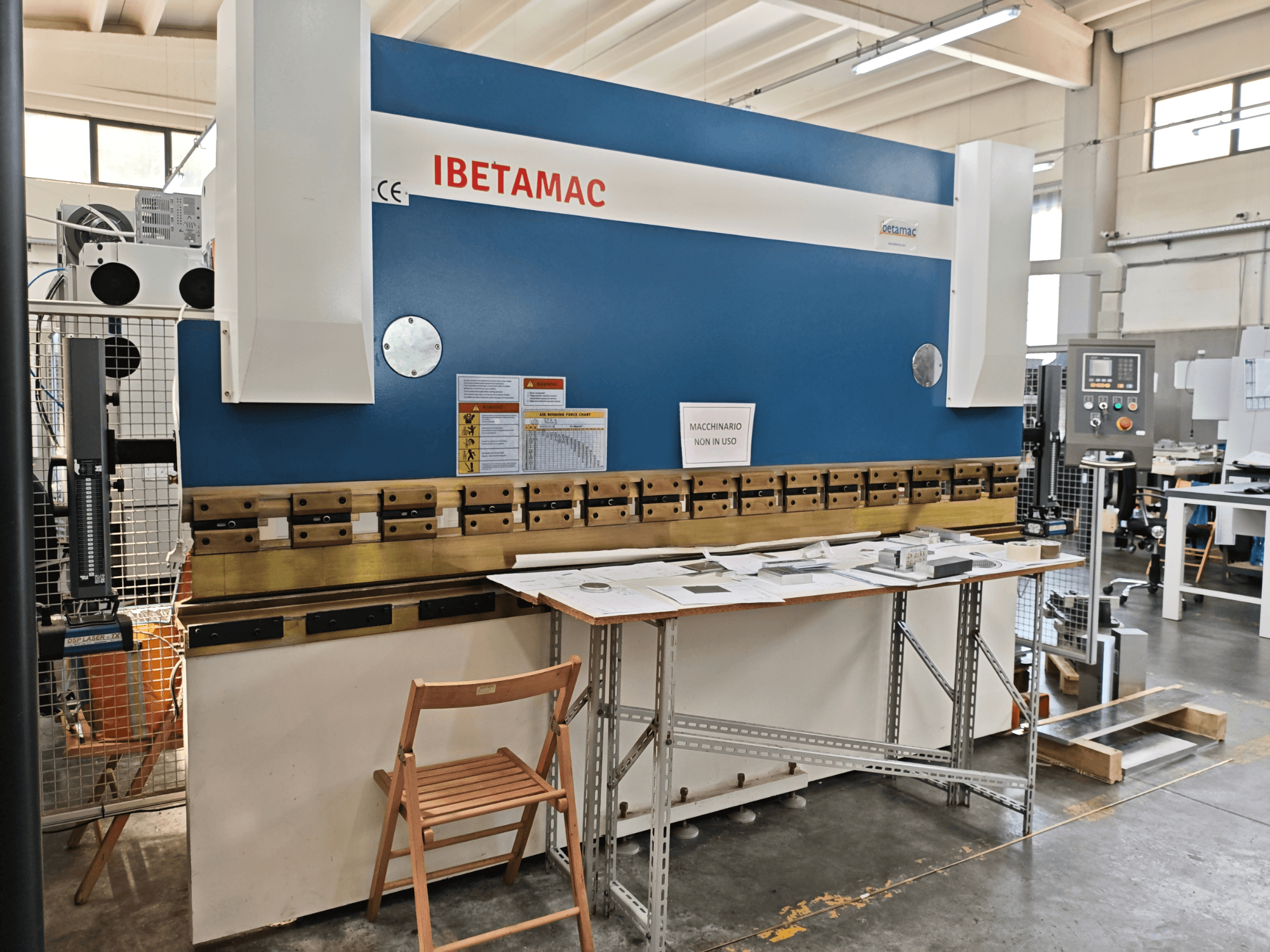 Гибочный пресс IBETAMAC 3200 100T в цехе, вид сбоку, на котором видны панель управления, рабочая зона и предупреждающие надписи.